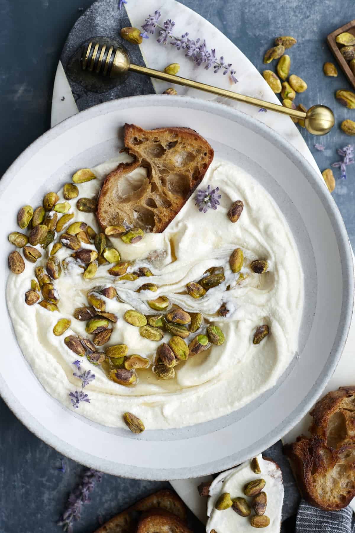 a bowl of whipped ricotta topped with honey and pistachios with a piece of crostini on top