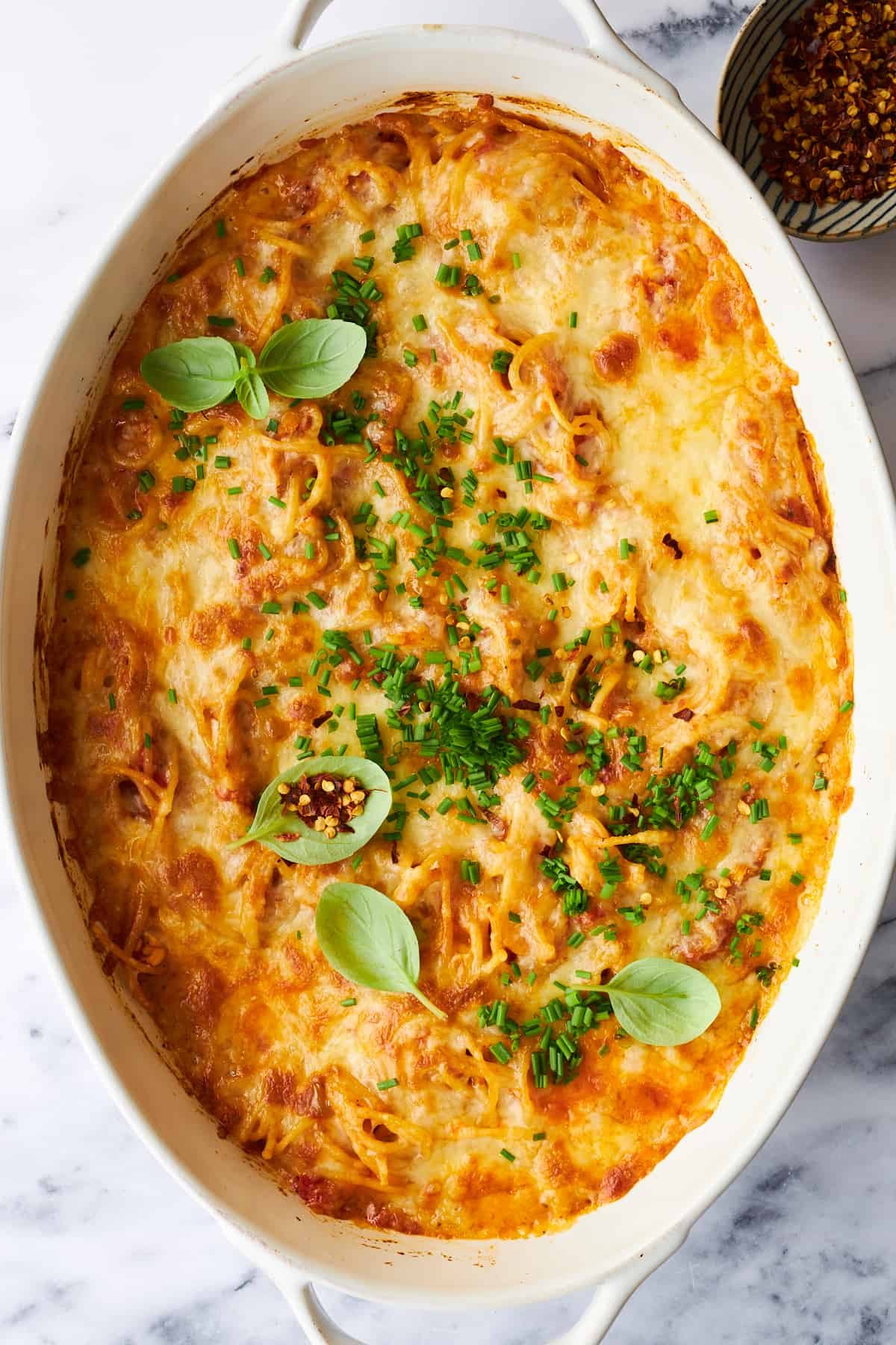 Cheesy baked spaghetti in an oval baking dish.