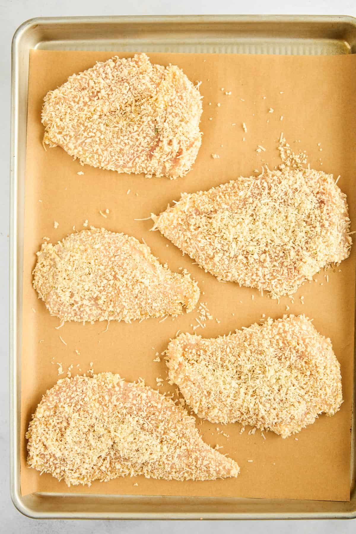 Raw breaded chicken pieces on a baking sheet.