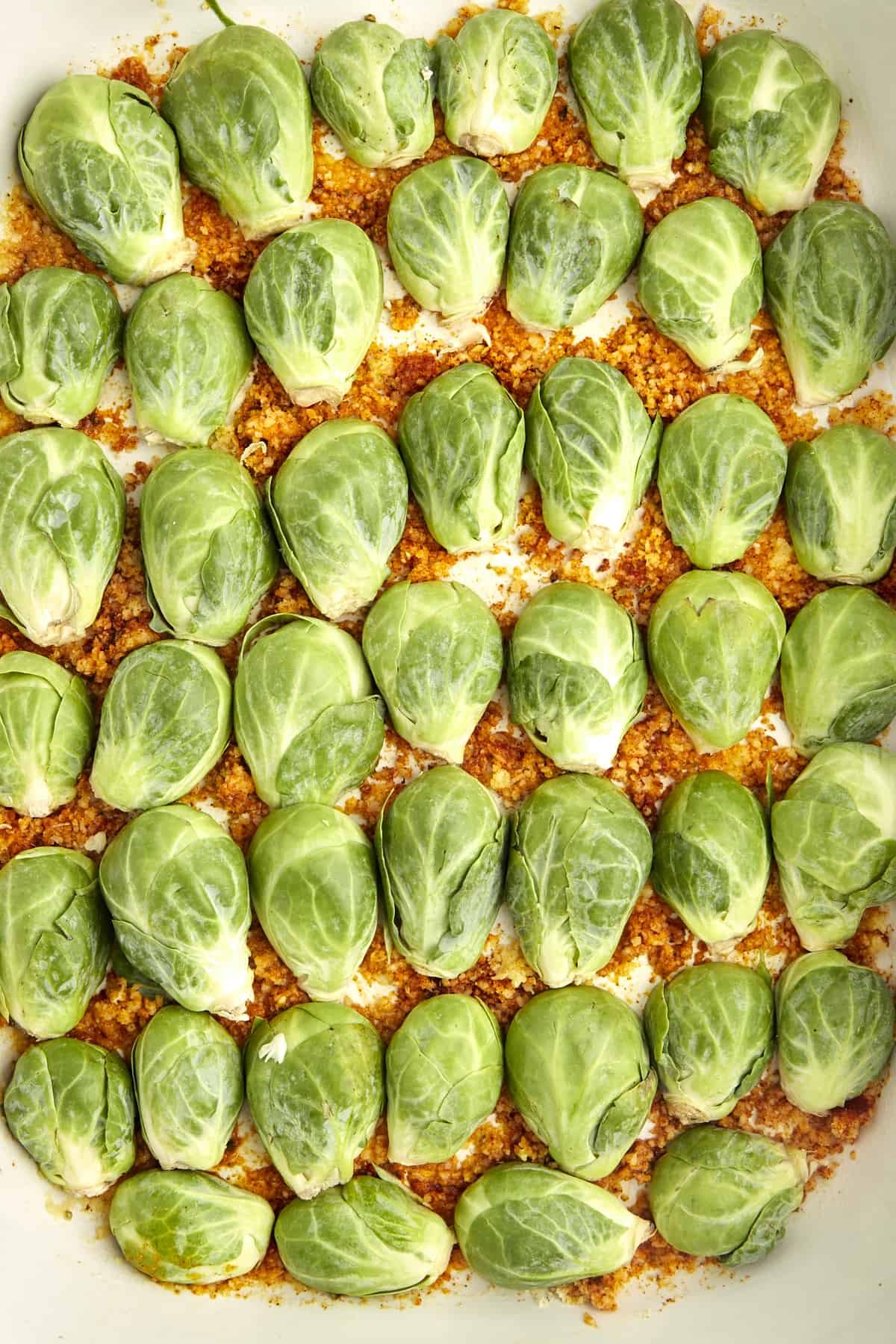 Halved Brussels sprouts in a baking dish on top of a layer of butter, spices, and Parmesan.