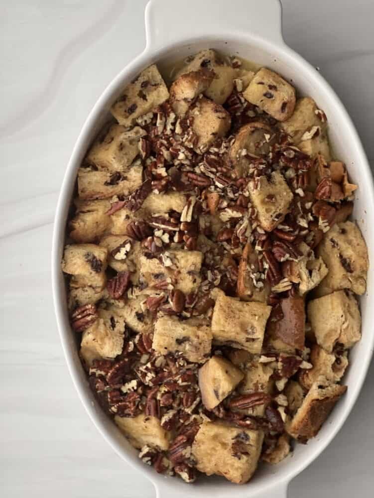 overhead image of unbaked panettone bread pudding with pecan pie filling in an oval baking dish.