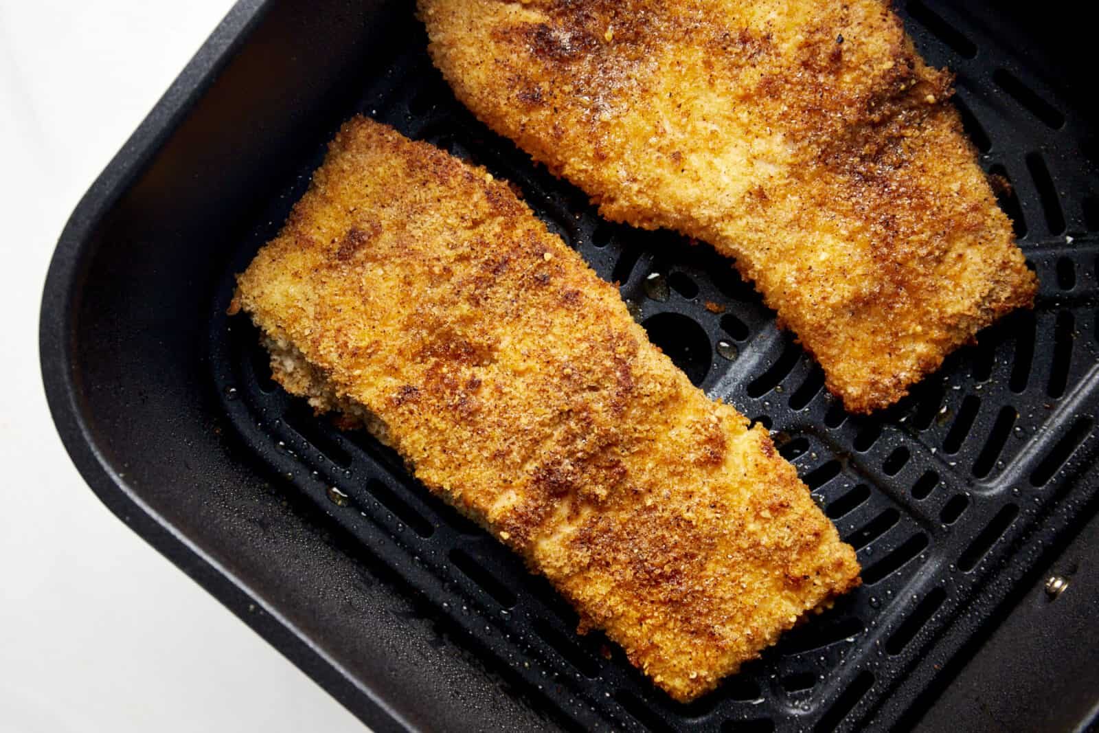 Two cooked Parmesan salmon filets in an air fryer basket.