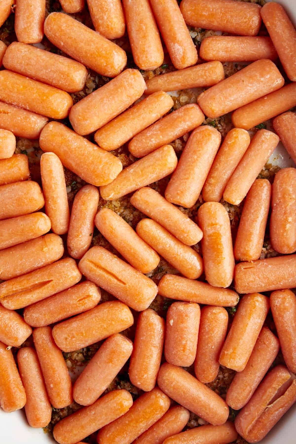 Raw baby carrots in a baking dish on top of a butter, panko, Parmesan coating.