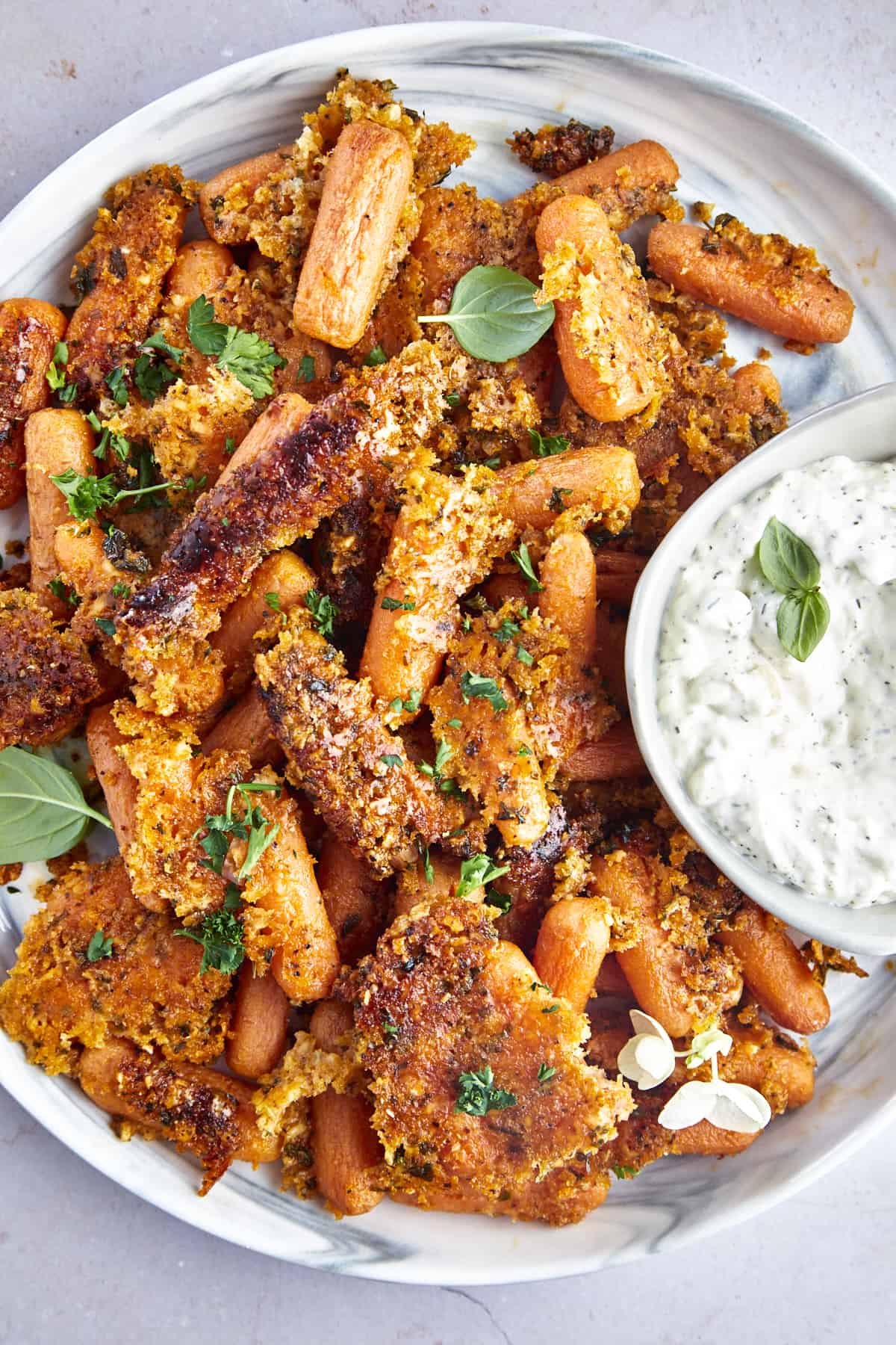A serving platter full of Parmesan oven roasted carrots with a bowl of tzatziki on the side.