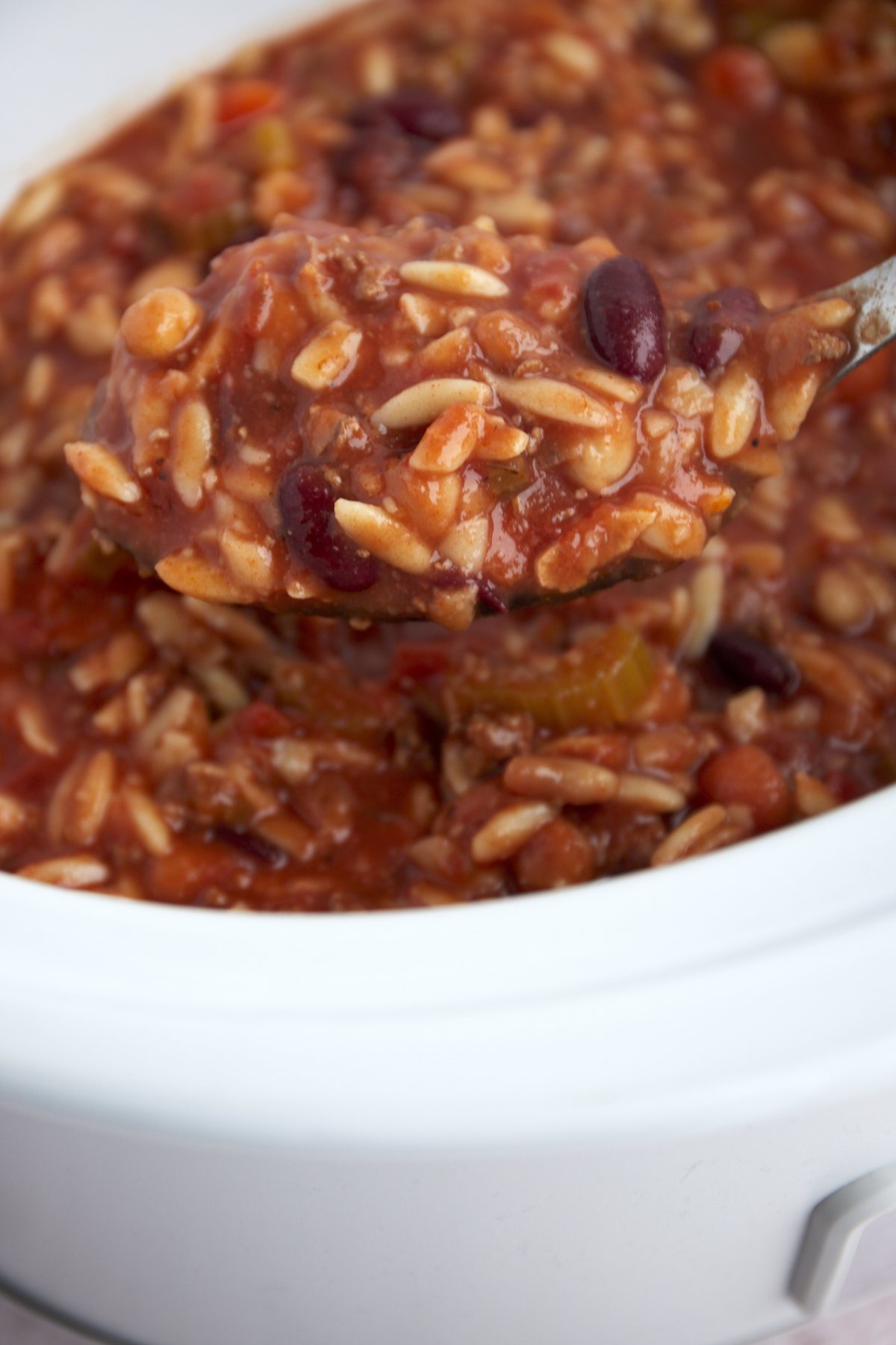 a spoon of pasta and beans soup being lifted from a slow cooker.