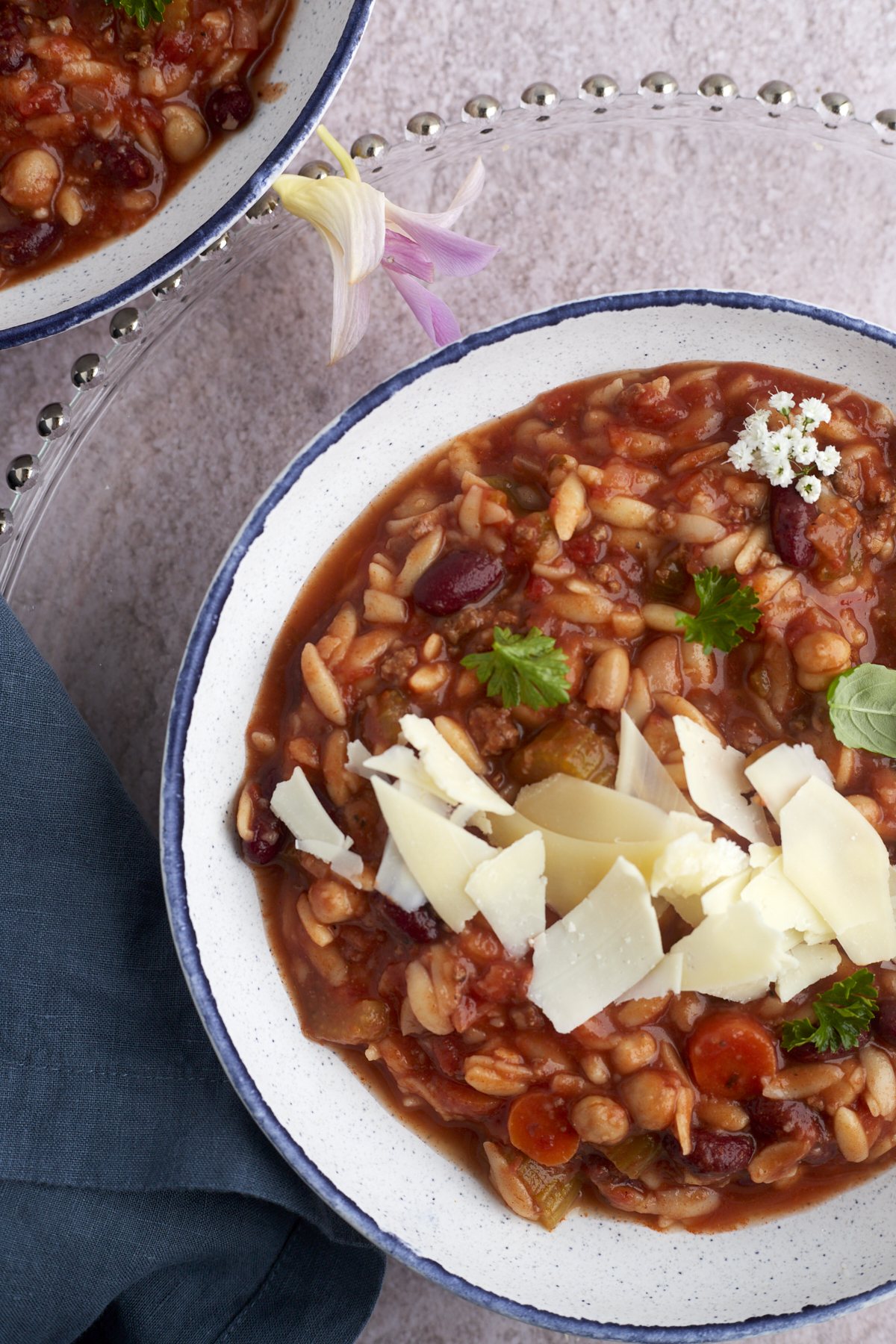 a bowl of pasta and beans soup topped with shaved Parmesan cheese.