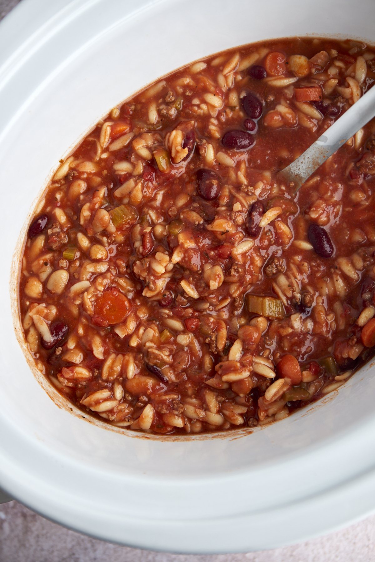 overhead image of pasta and beans soup in a slow cooker.