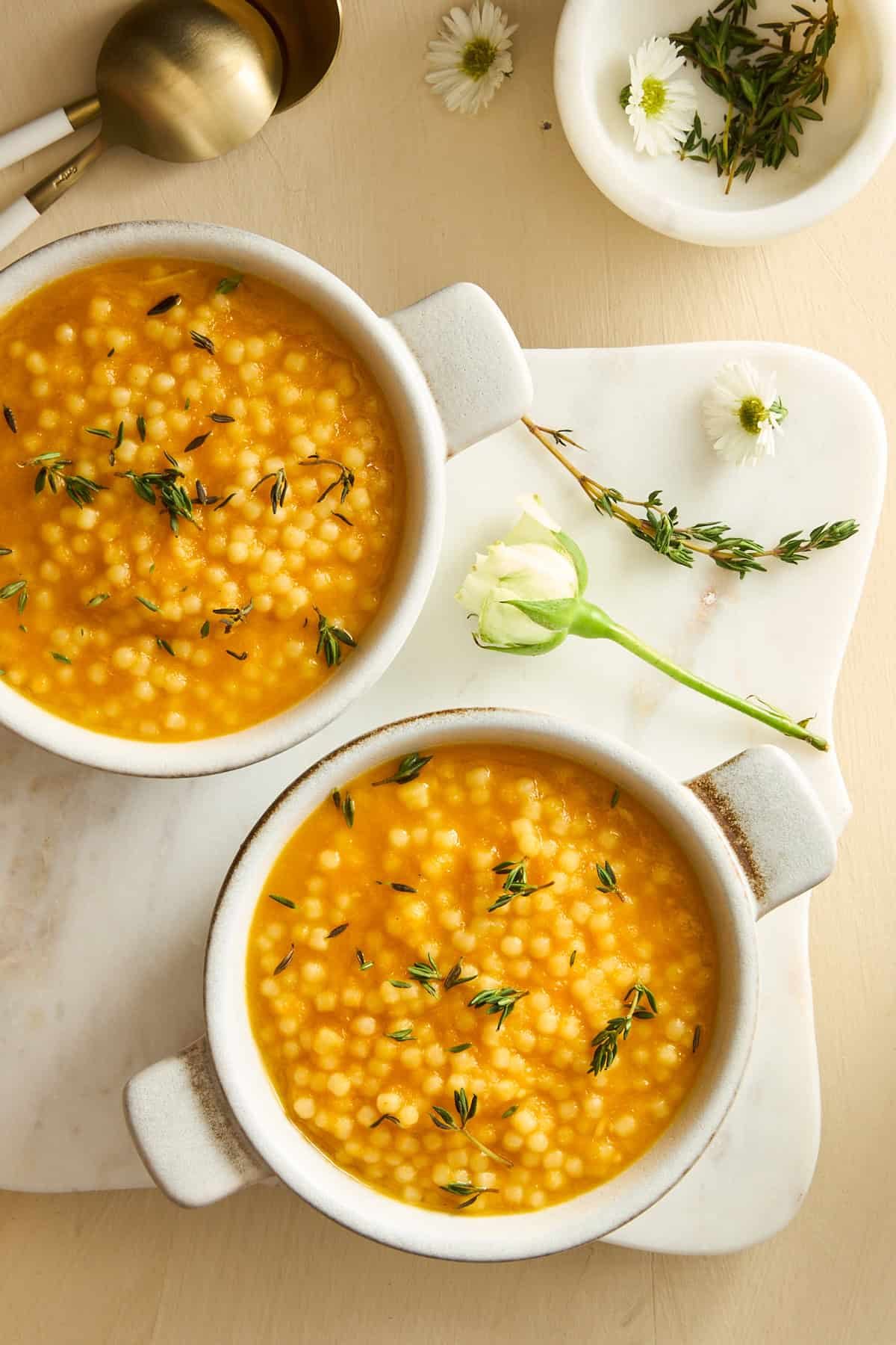 Two bowls of pastina soup topped with rosemary.