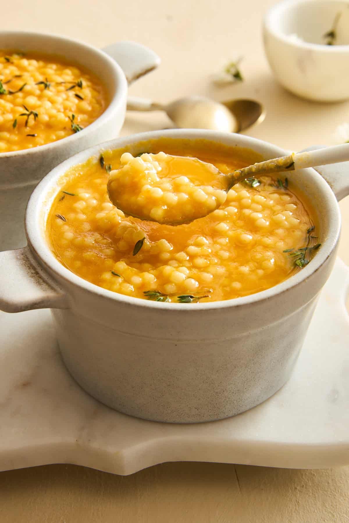 A spoon lifting a bite of pastina soup from a bowl.