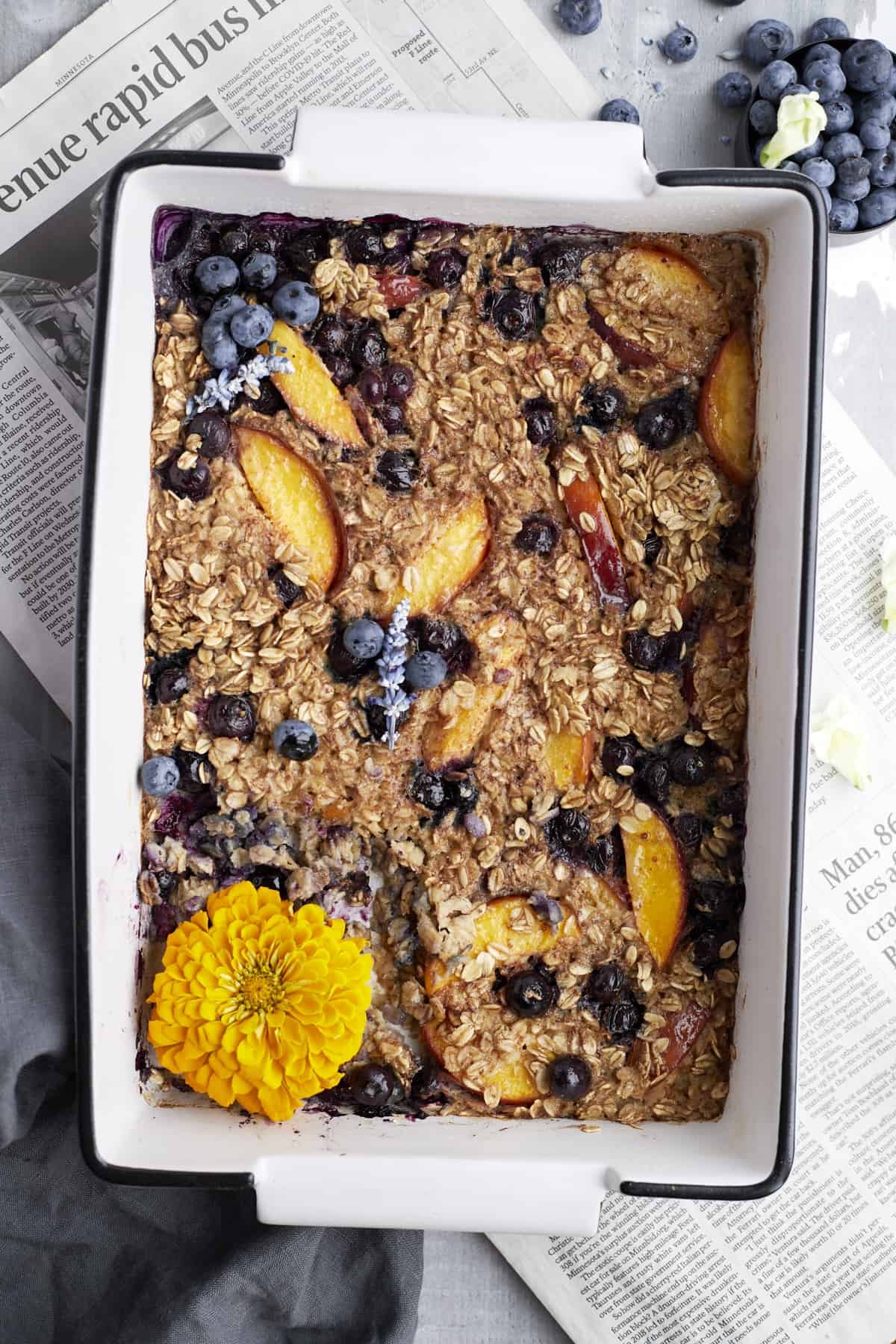 overhead image of peach blueberry baked oats in a baking dish over newspaper