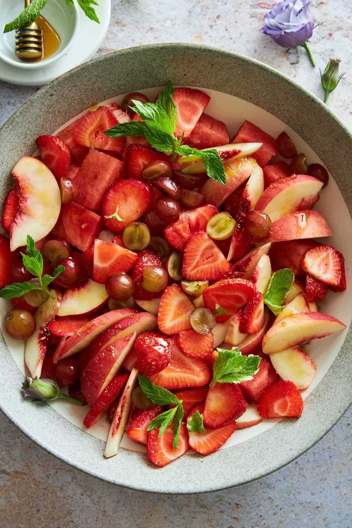 A bowl of peach watermelon salad with grapes, strawberries, and mint.