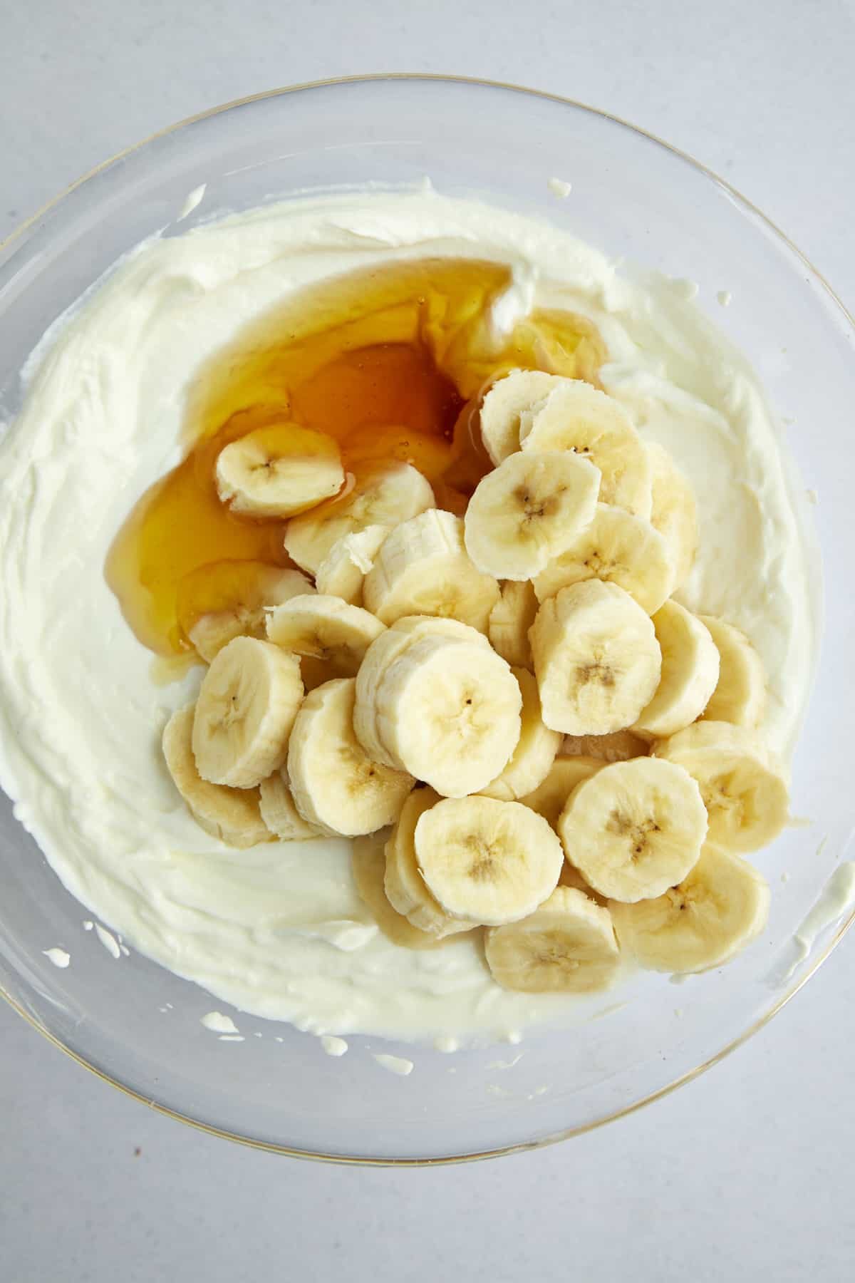 Overhead image of plain Greek yogurt, honey, and banana coins in a large mixing bowl.