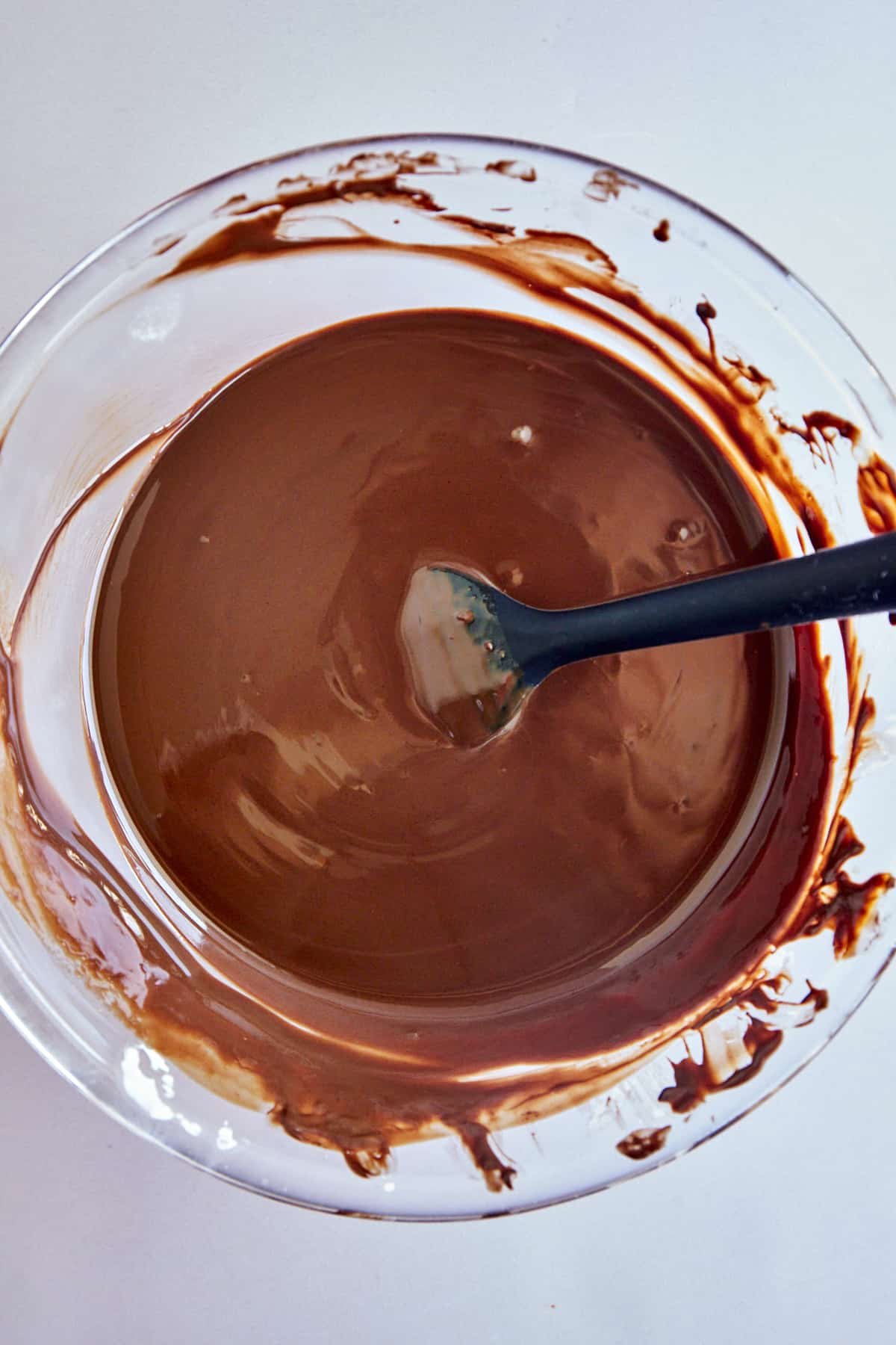 Overhead image of a bowl of melted chocolate with a rubber spoon sticking out.