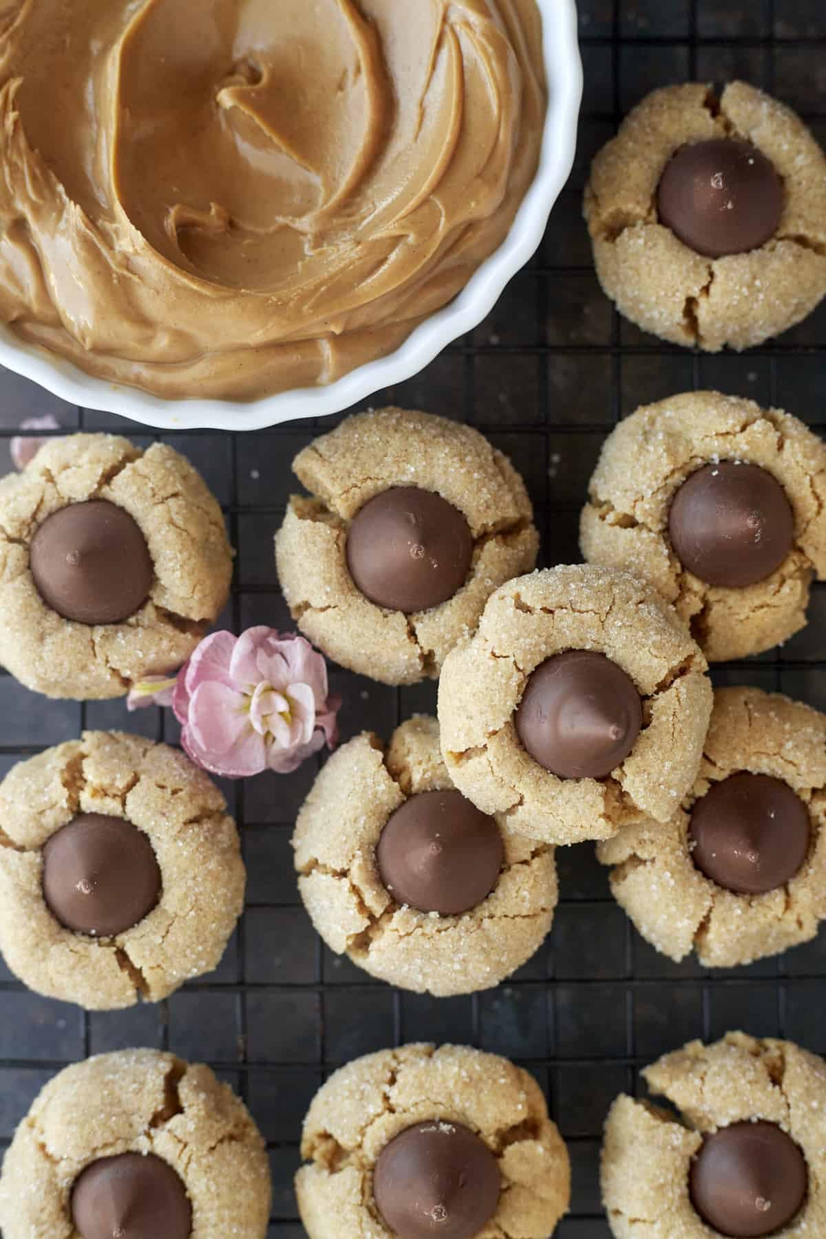 peanut butter blossoms on a cooling rack with a bowl of peanut butter on the side.