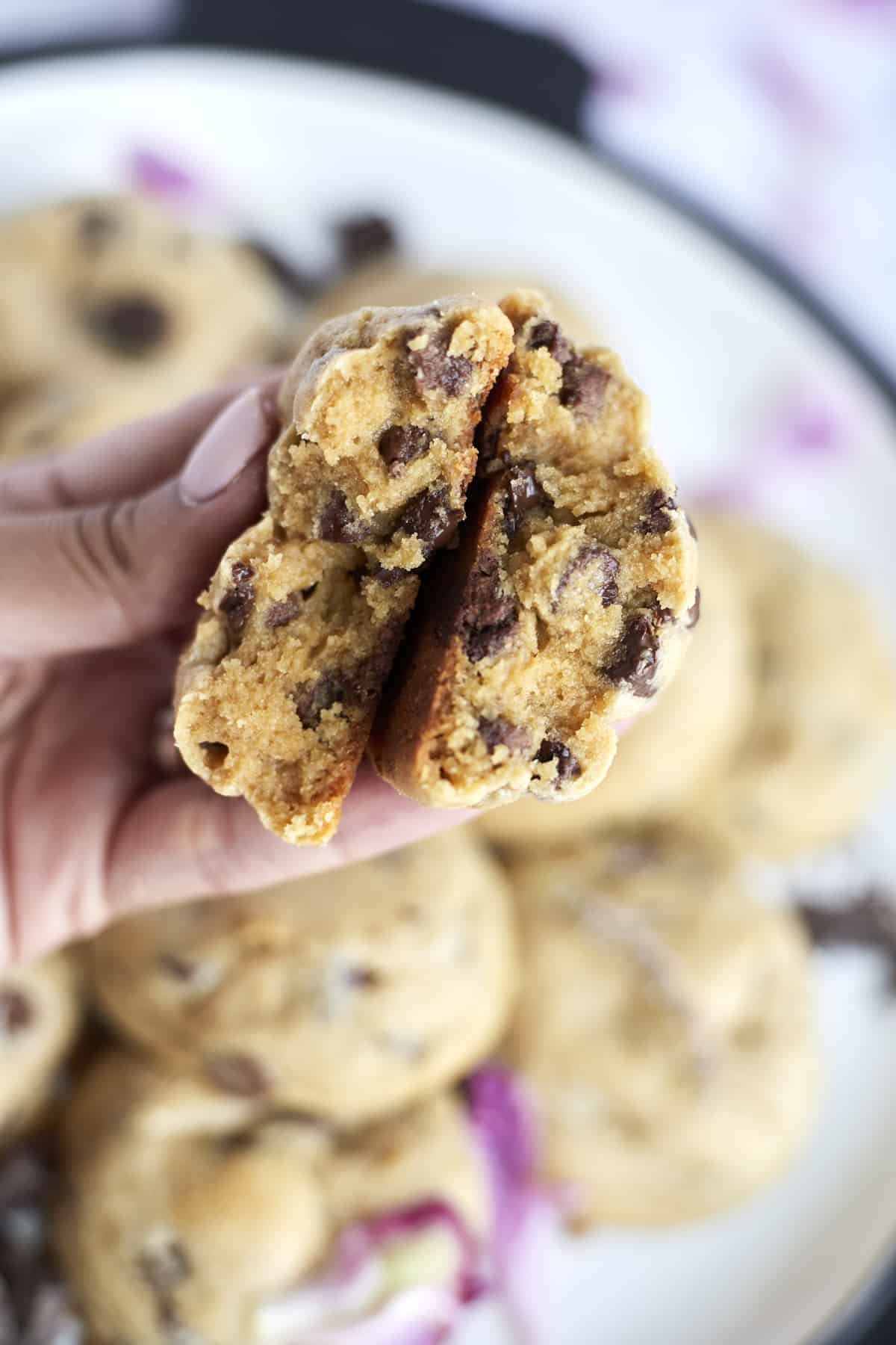 a hand holding two halves of a peanut butter chocolate chunk cookies showing the center.