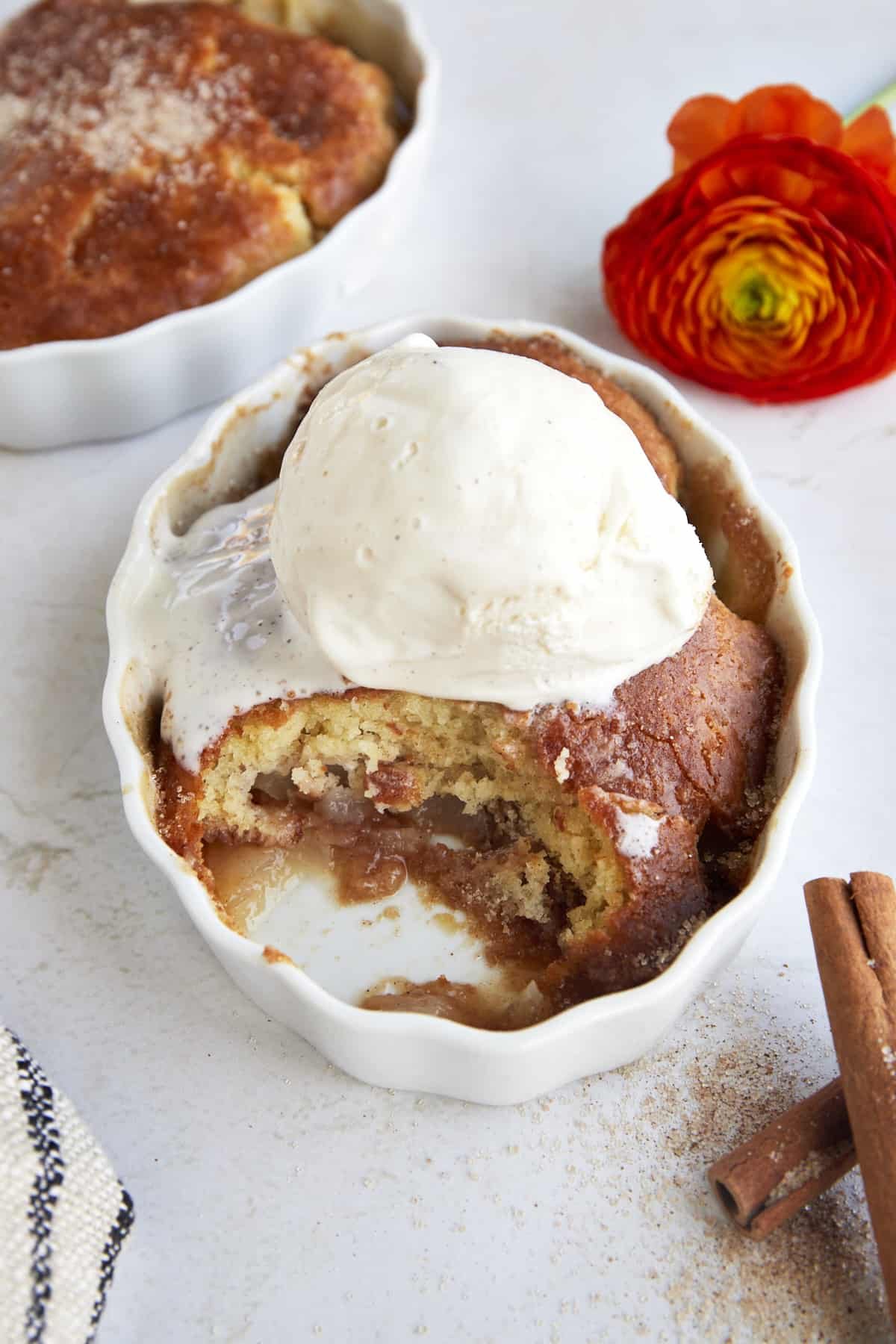 A ramekin of pear cobbler topped with ice cream with a bite missing.