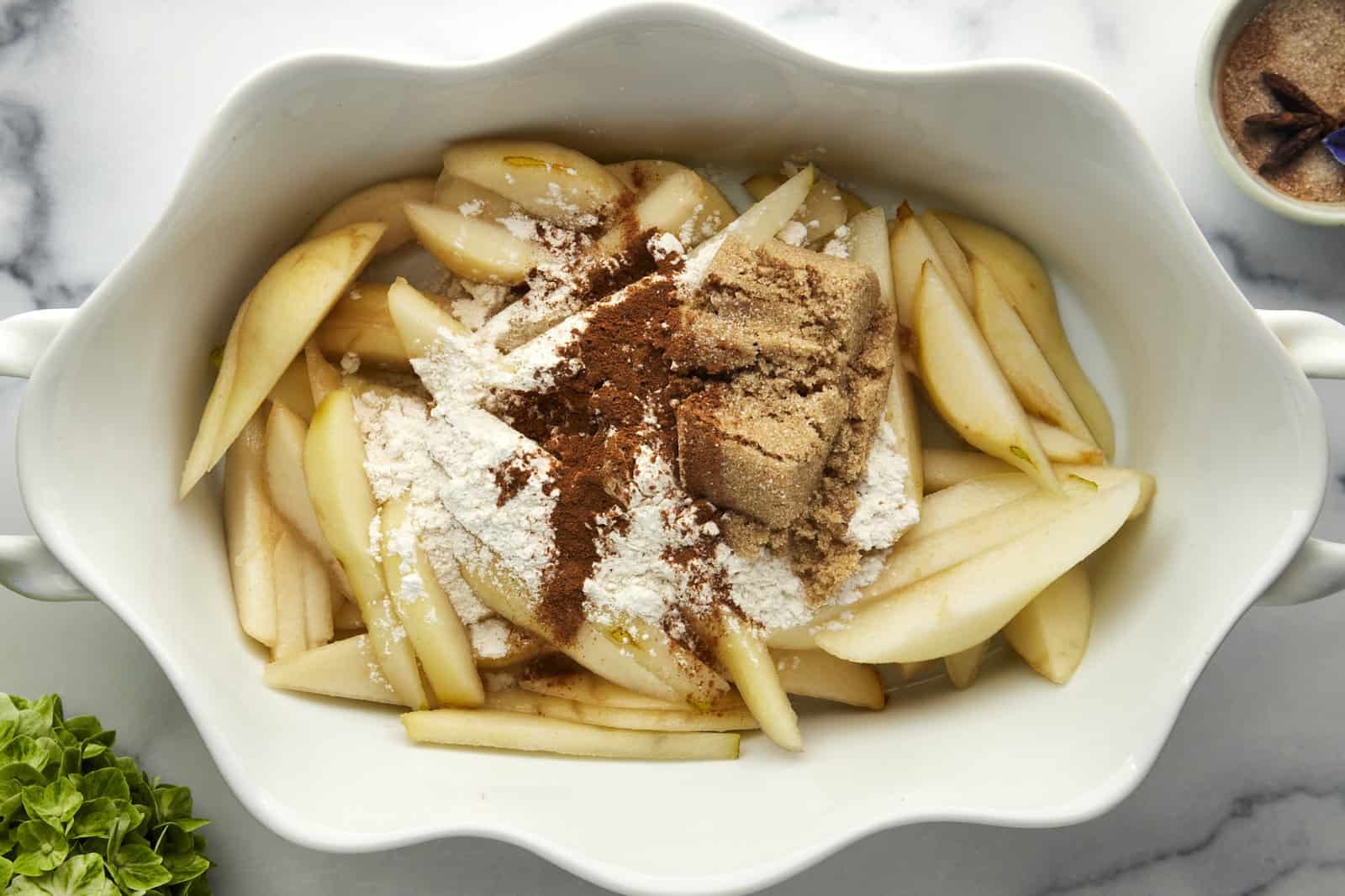 Pears in a baking dish topped with flour, brown sugar, and cinnamon.