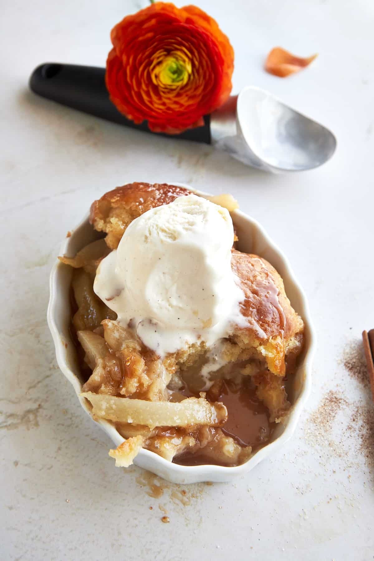 A serving of pear cobbler in a dish topped with vanilla ice cream with a bite missing.