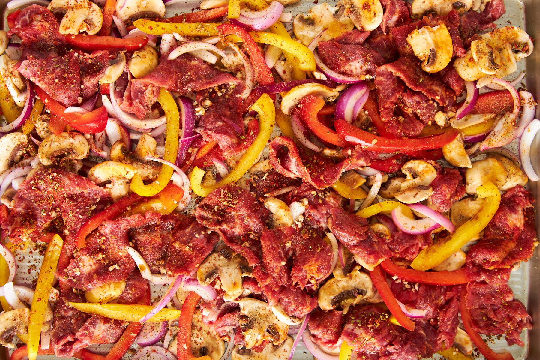 Uncooked Philly cheesesteak ingredients on a baking sheet.