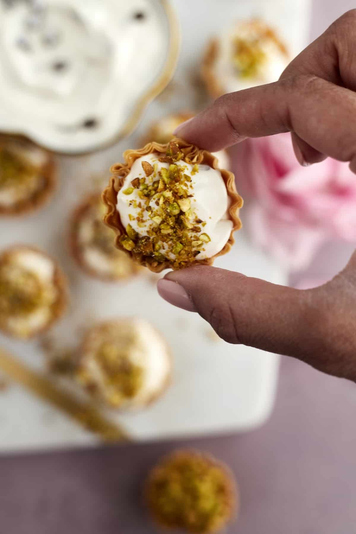 two fingers holding a phyllo cup cannoli bite topped with pistachios