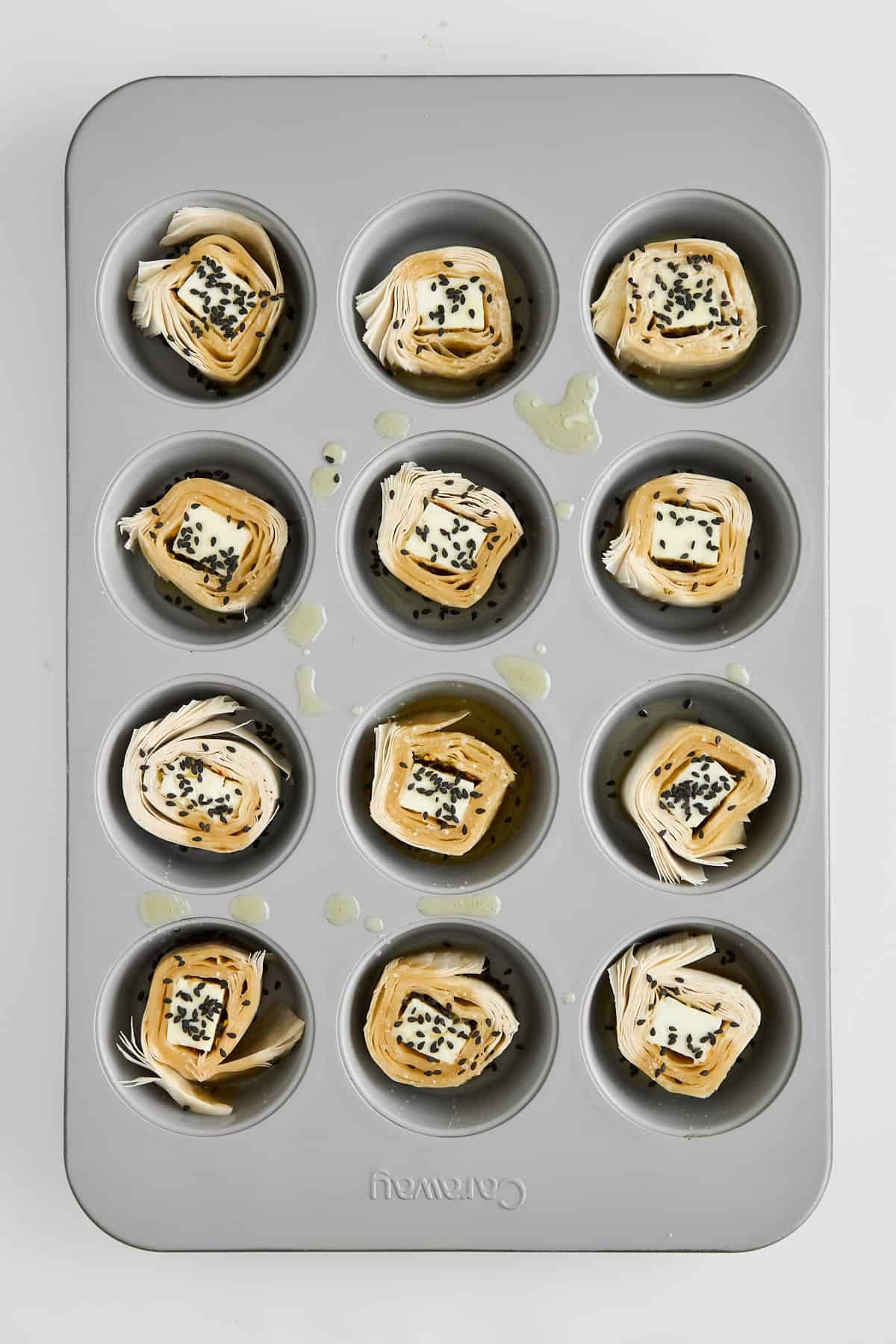 Hot Honey Feta Phyllo Rolls in a muffin pan topped with butter.