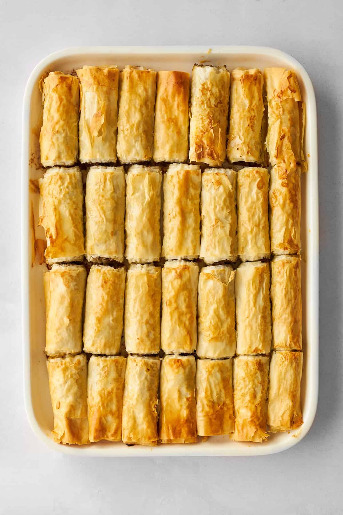 A baking dish full of stuffed phyllo rolls with ground beef.