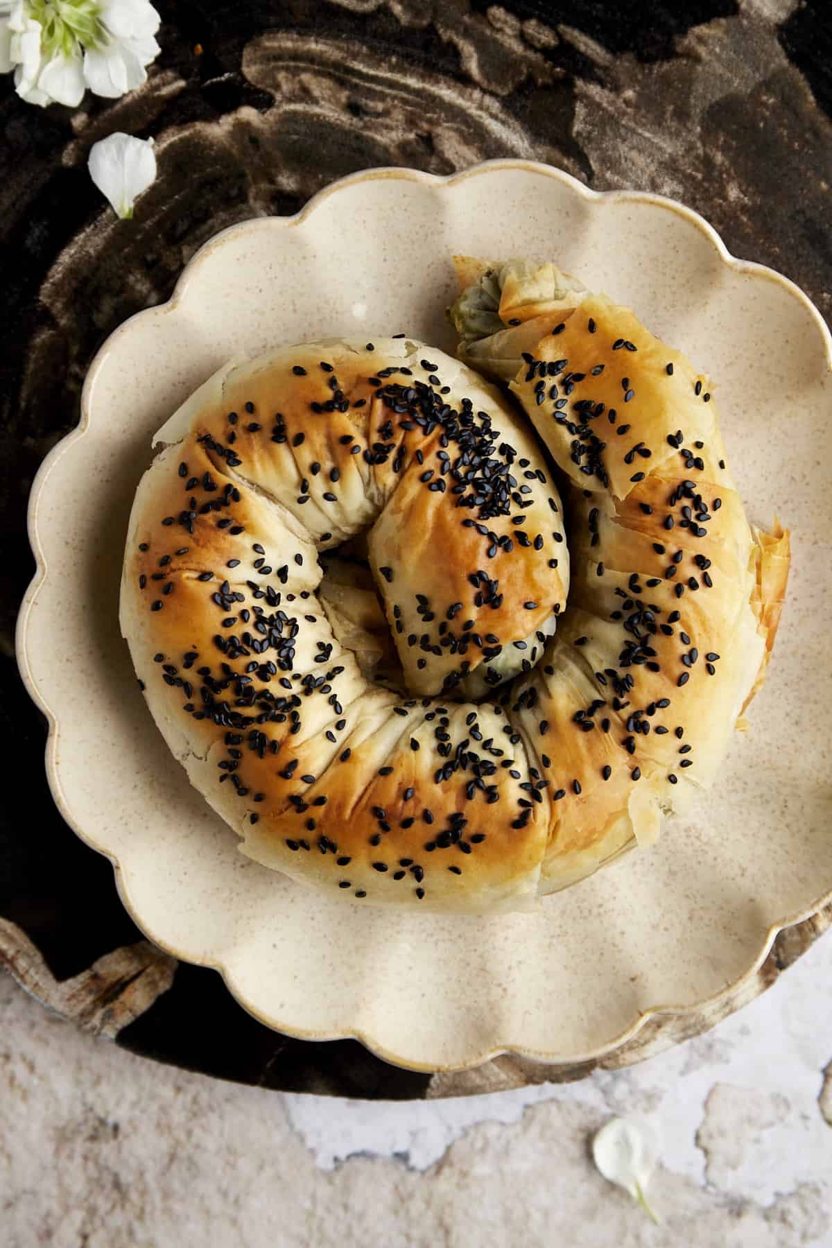 A phyllo spanakopita roll topped with back sesame seeds on a plate.