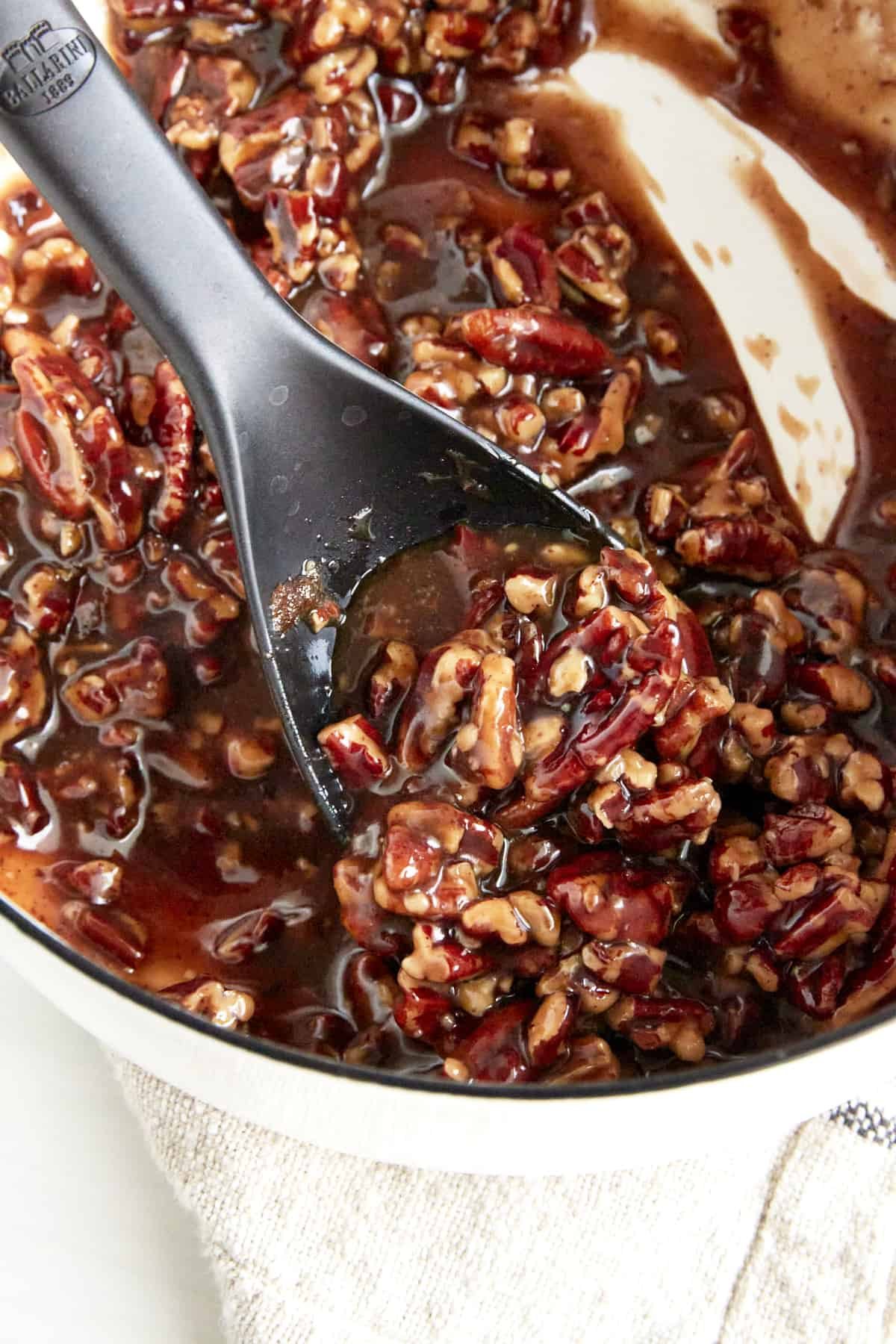Pecan pie filling in a saucepan being stirred with a spoon.