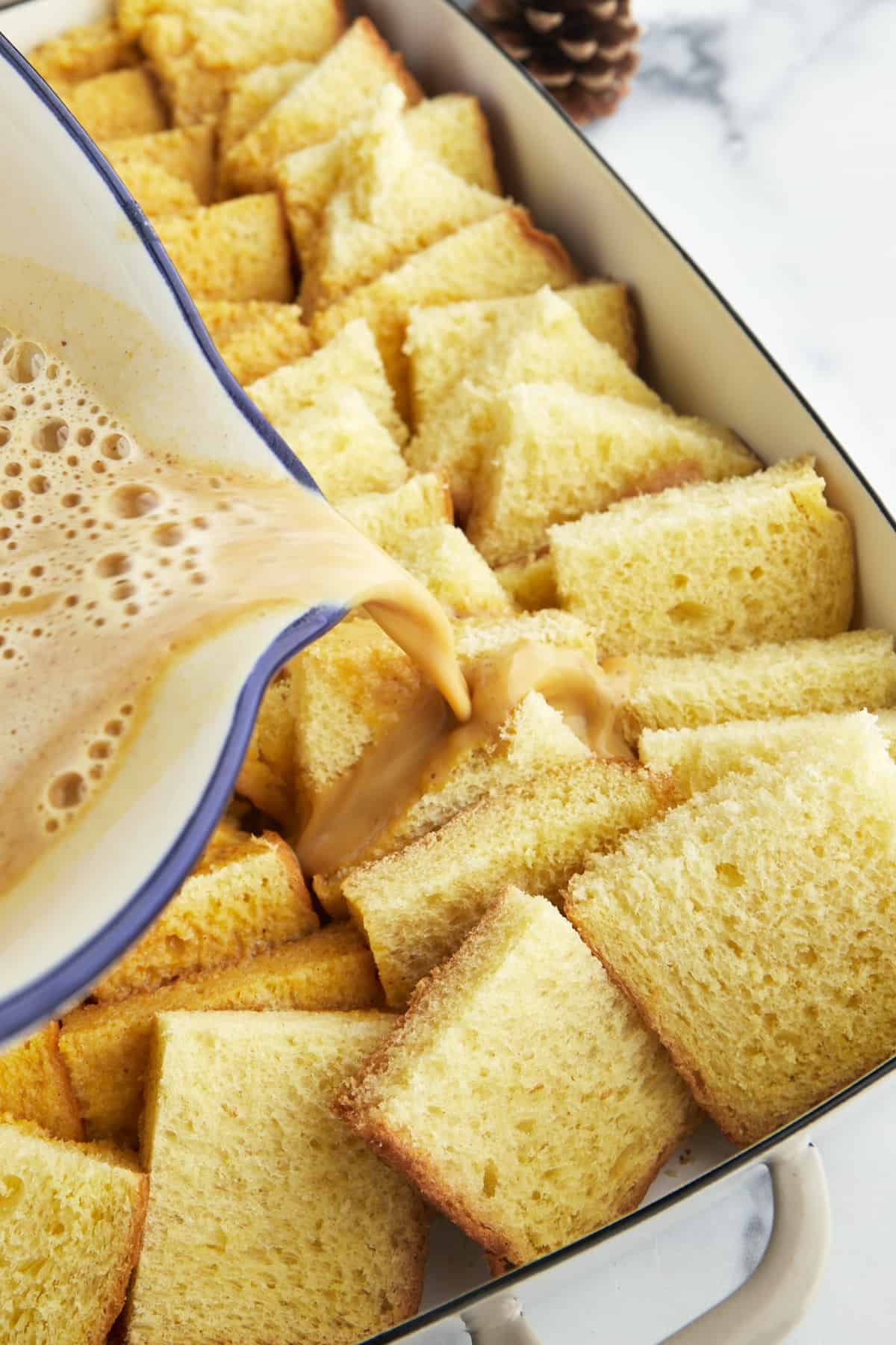 Pumpkin custard being poured over bread pieces in a baking dish.