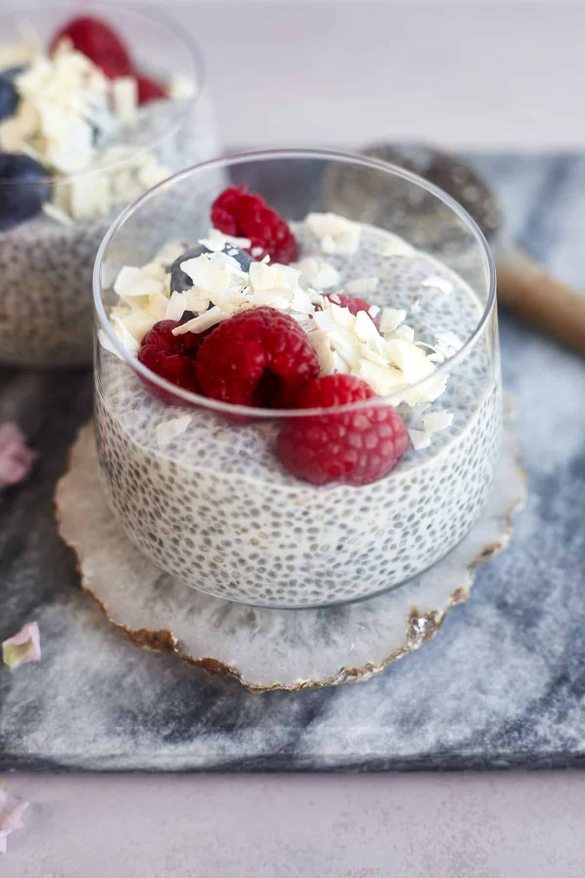 a jar of coconut chia pudding topped with fresh raspberries and coconut flakes - great Ramadan recipe