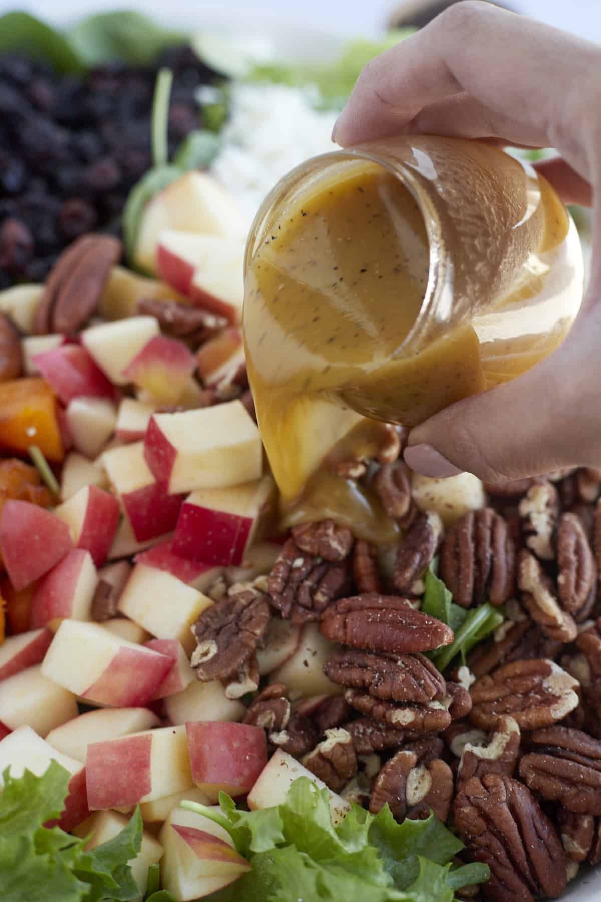 a hand drizzling dijon salad dressing over roasted butternut squash salad