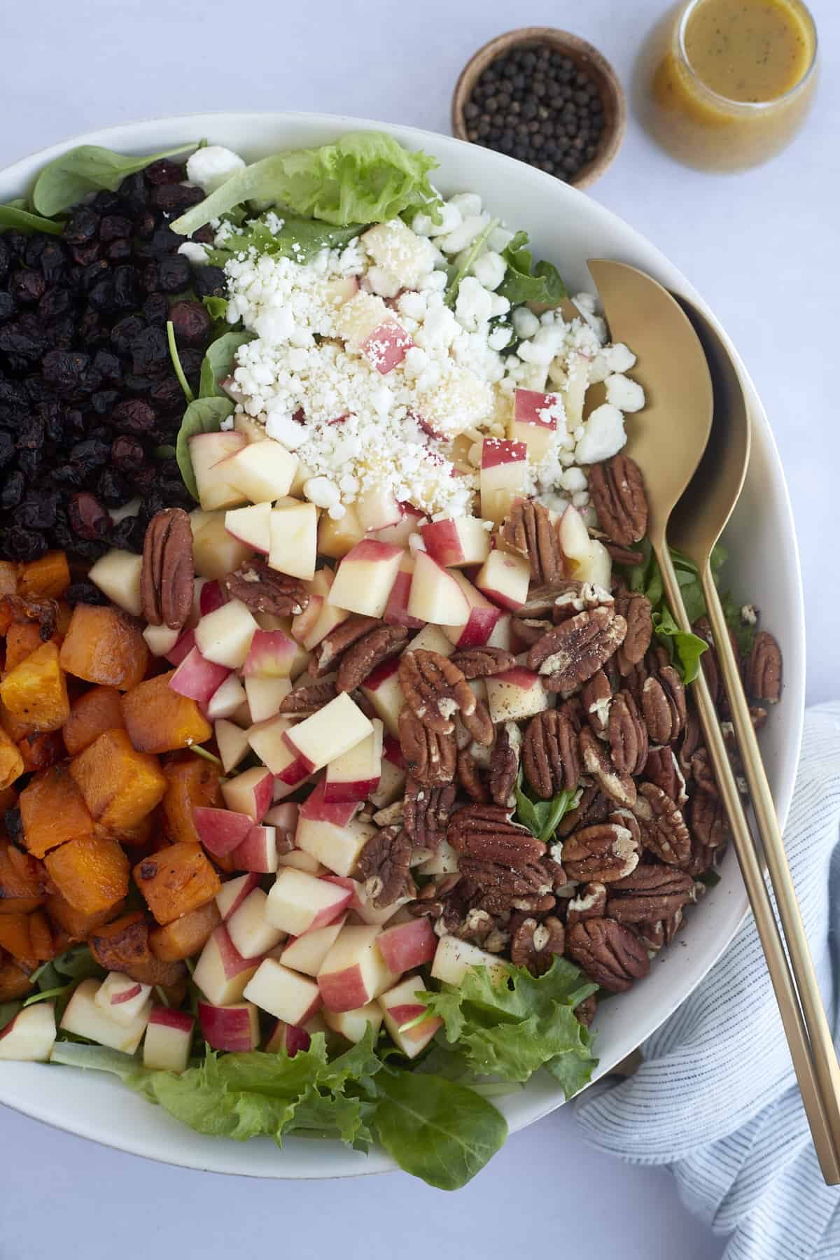 a bowl of roasted butternut squash salad with butternut squash, dried cranberries, apples, goat cheese, and pecans