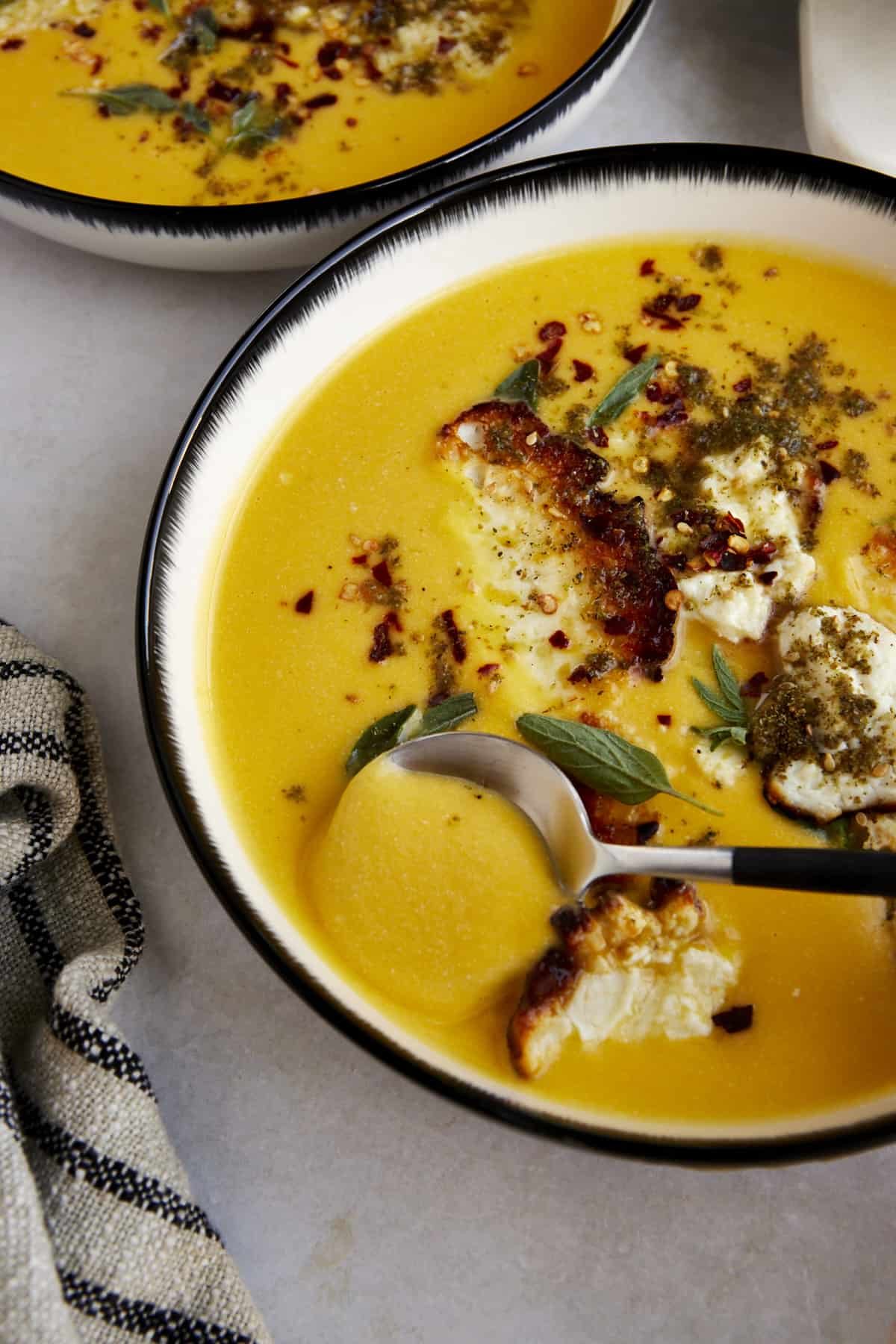 A spoon scooping a bite of roasted butternut squash soup with feta crisps.