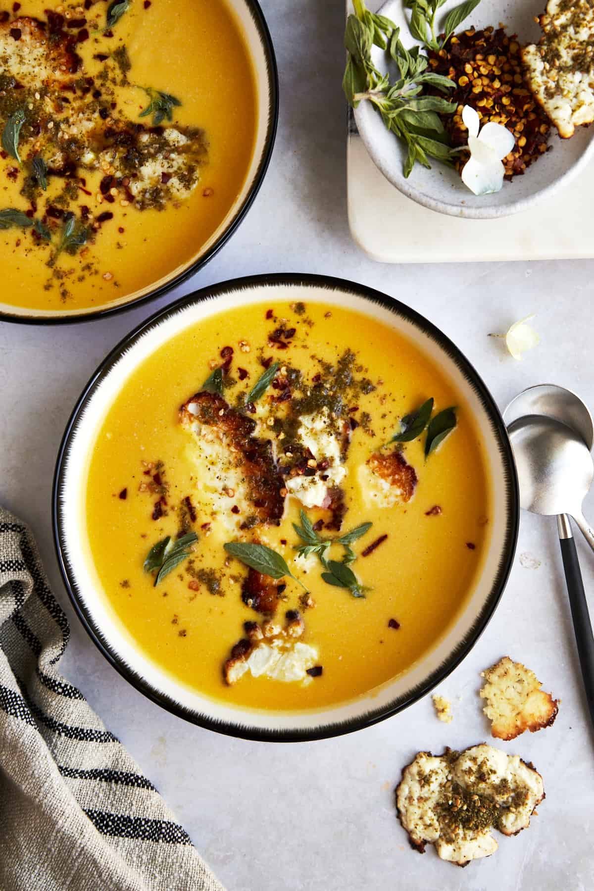 Two bowl of roasted butternut squash soup topped with feta crisps.