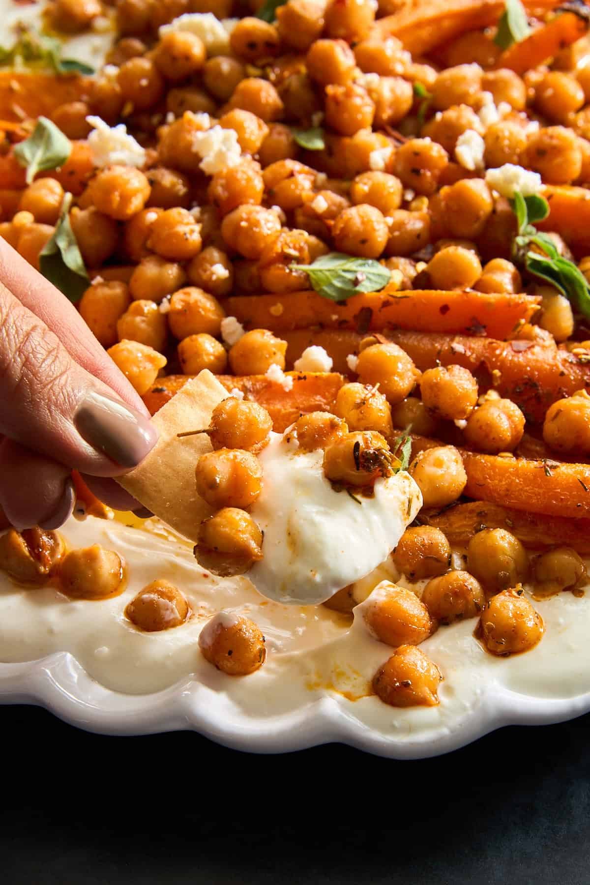 A hand dipping a pita chip into chickpeas and roasted carrot whipped feta.