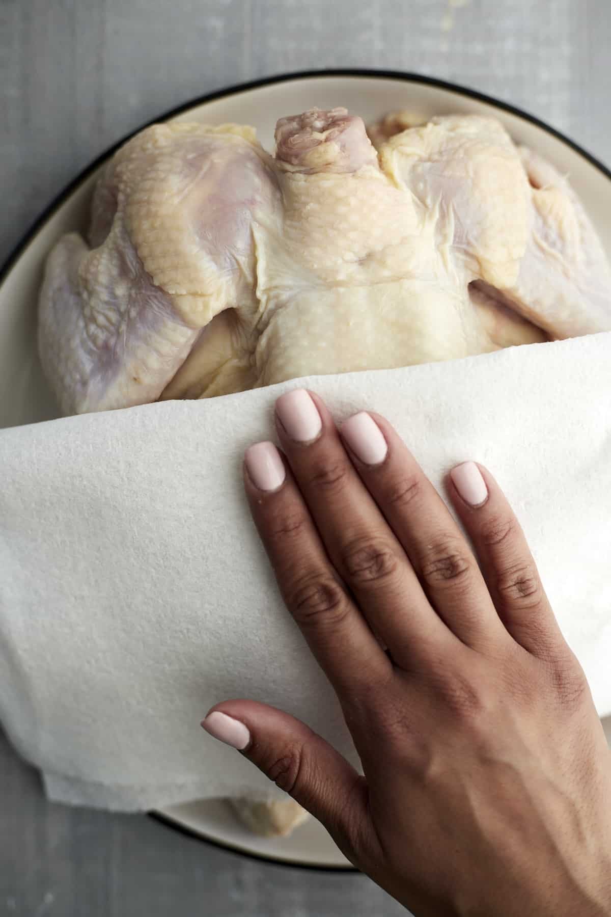 a hand using a paper towel to pat a whole raw chicken dry