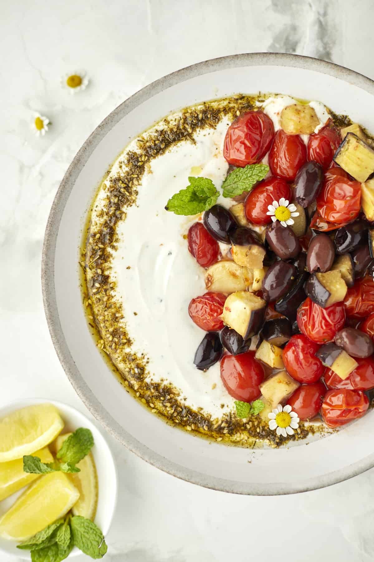 Roasted eggplant with tomatoes plated with silky yogurt dip and garnished withy zaatar