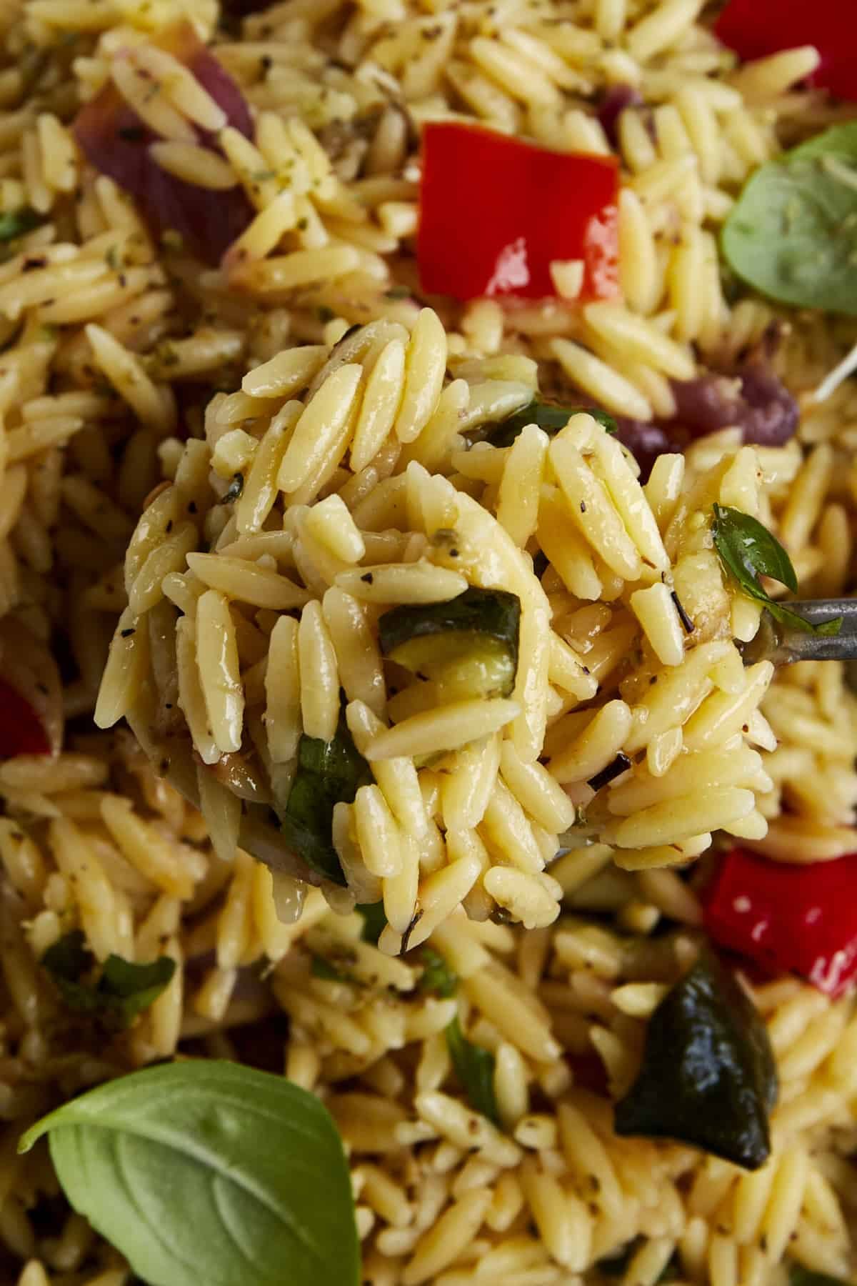 A spoon lifting up a bite of roasted veggie pasta salad.