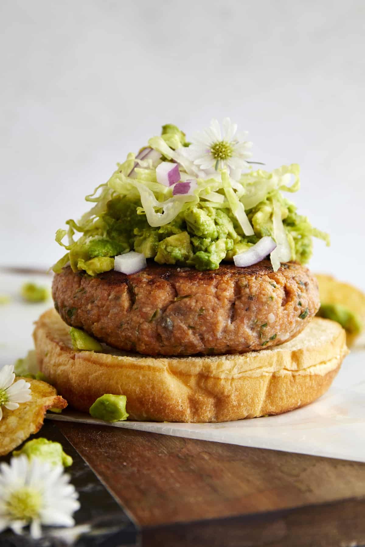 An open faced salmon burger with avocado, red onion, and lettuce.