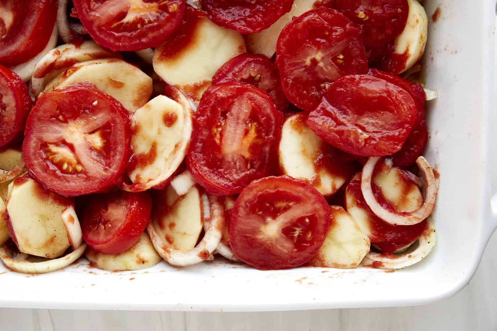 A baking dish with potatoes, onions, garlic, and tomatoes.