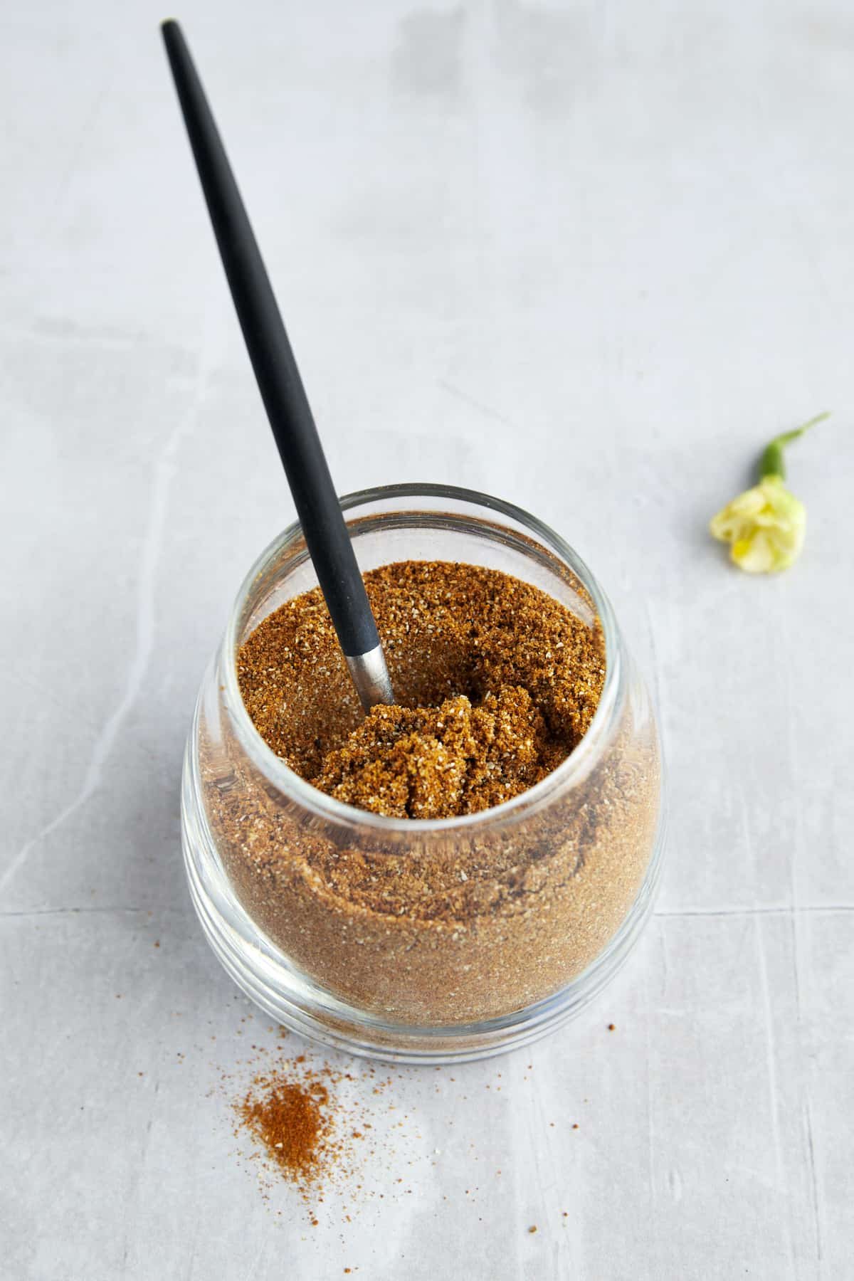 A jar of homemade shawarma seasoning with a spoon sticking out.