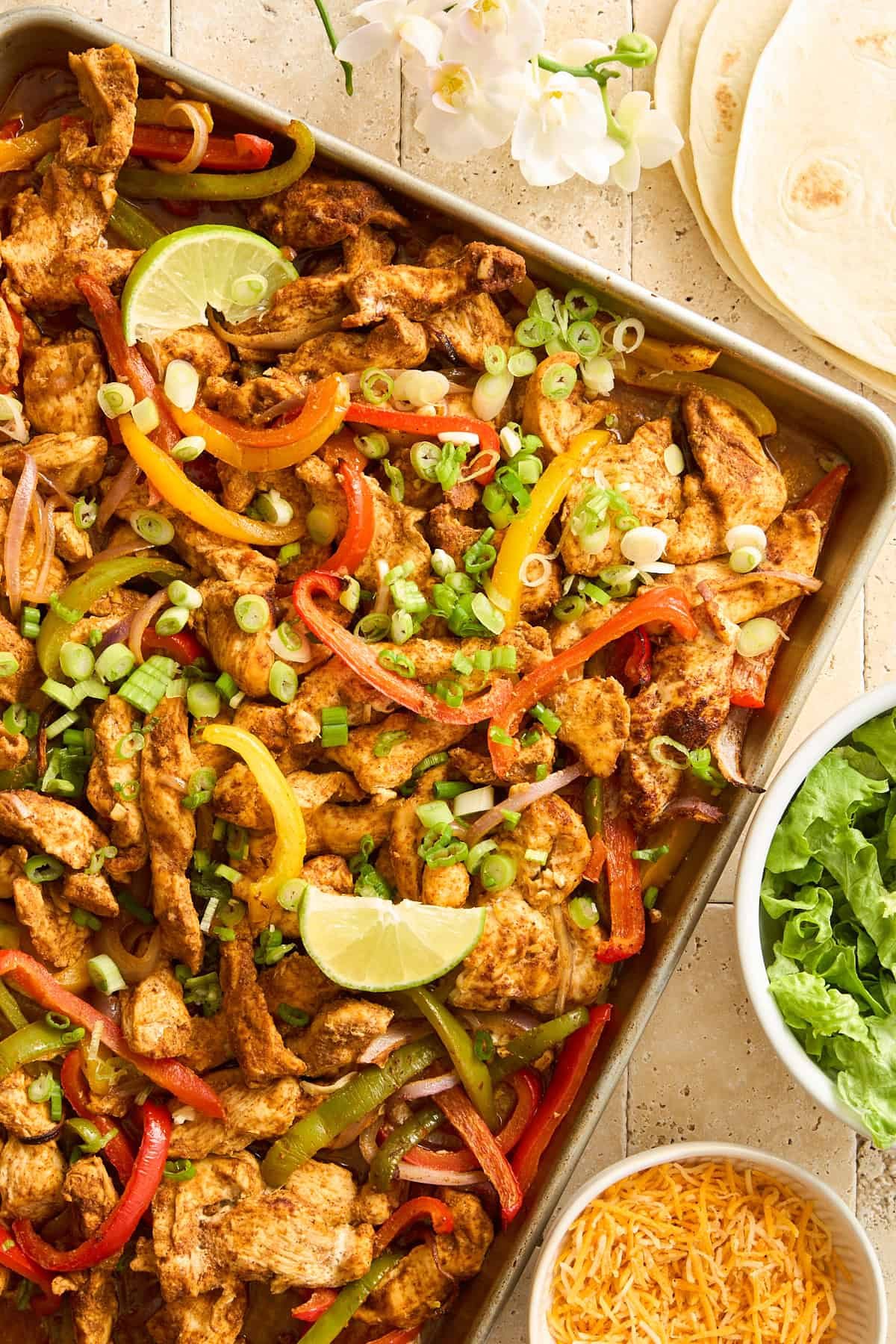 Sheet Pan Chicken Fajitas on a baking sheet topped with lime wedges.