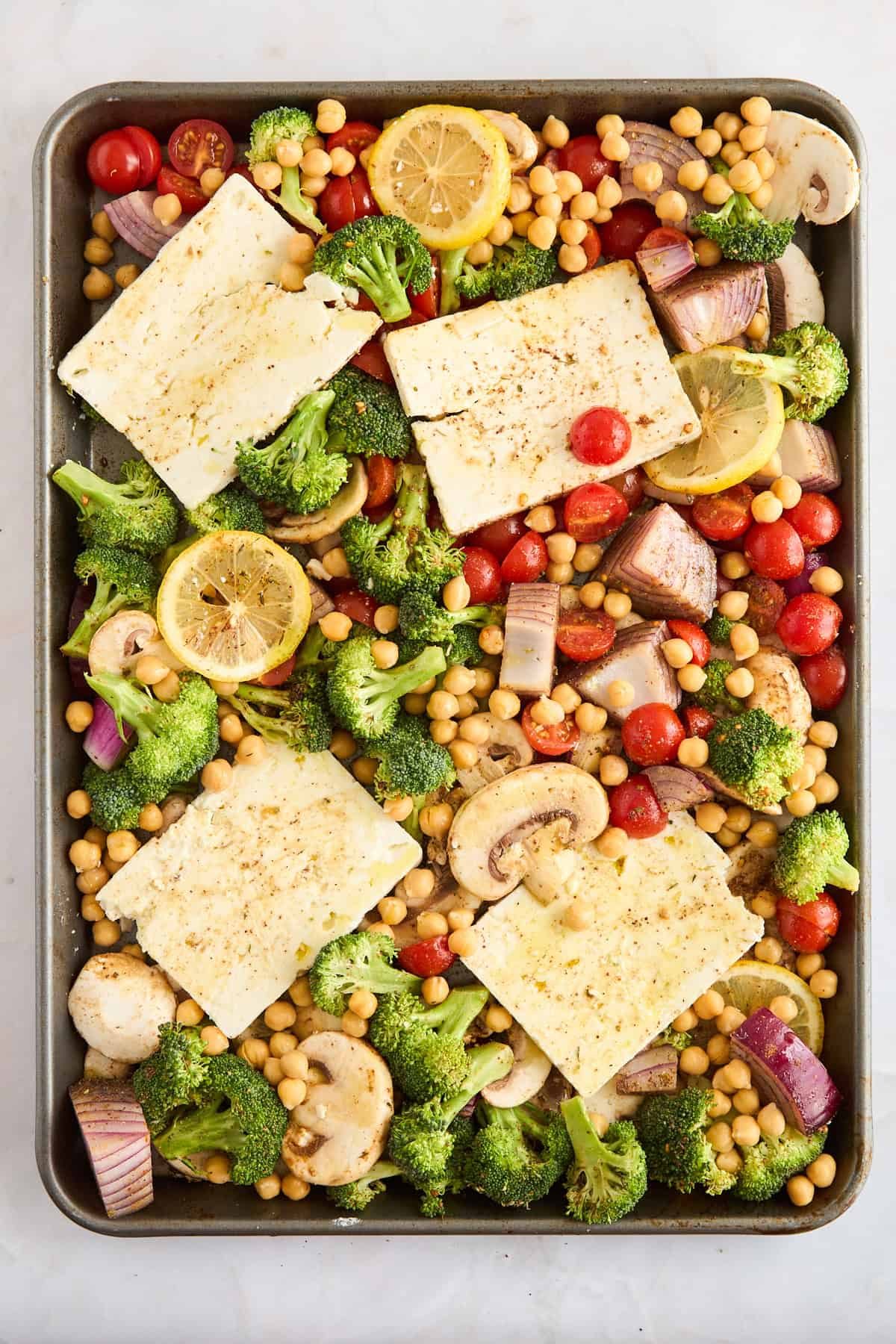 Seasoned raw veggies, feta, and chickpeas on a sheet pan.