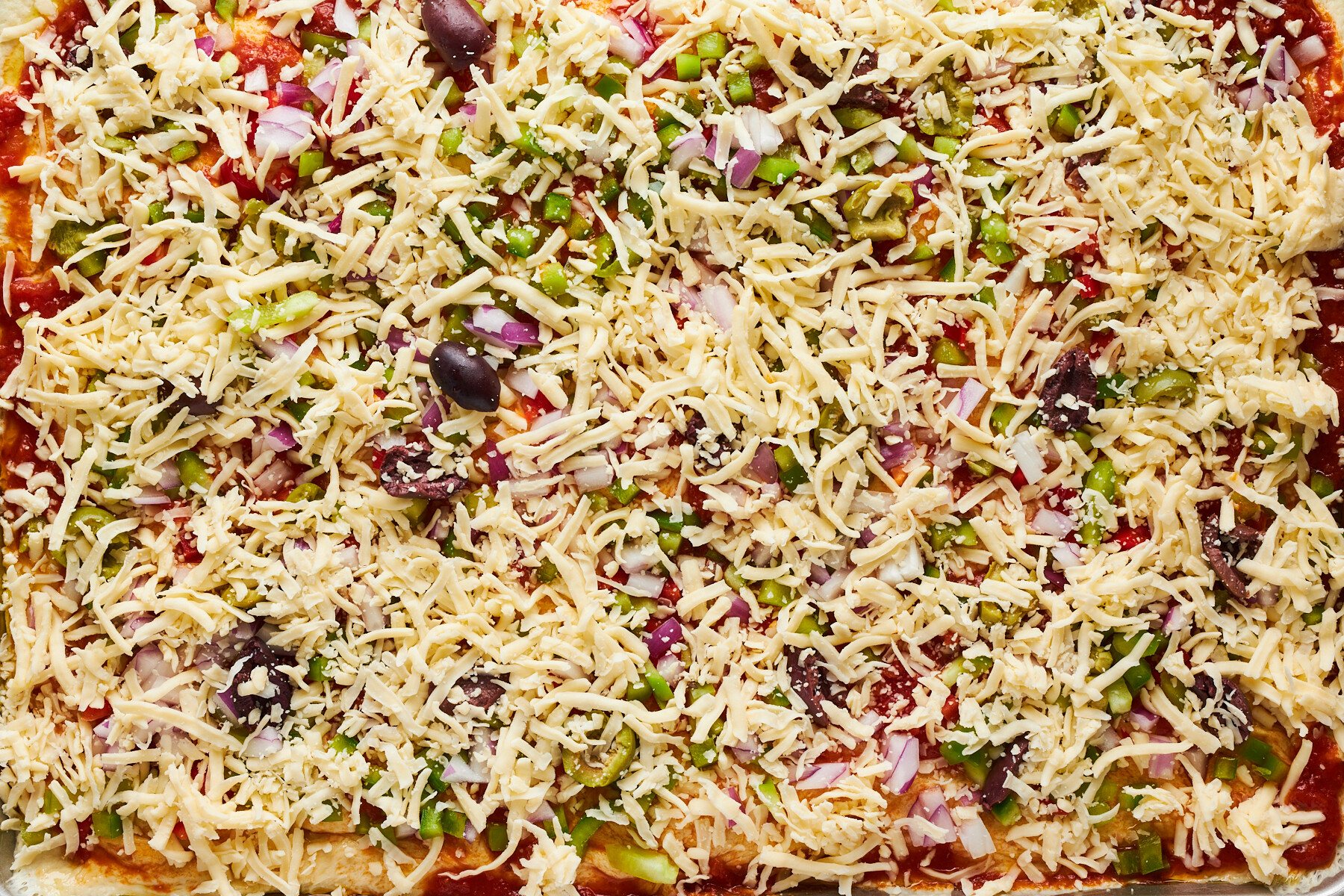 Raw dinner rolls topped with pizza sauce, chopped veggies, olives, and cheese.