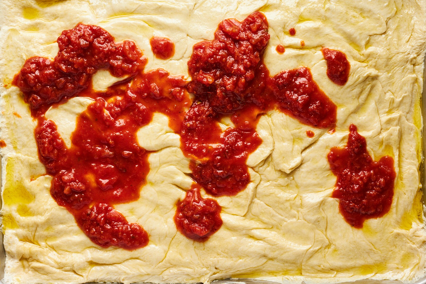Marinara sauce being spread over raw dinner rolls.
