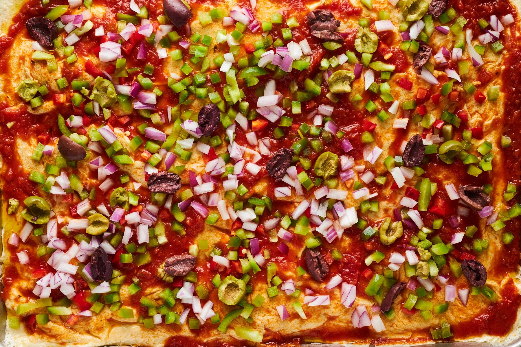 Raw dinner rolls topped with pizza sauce, peppers, onions, and olives.