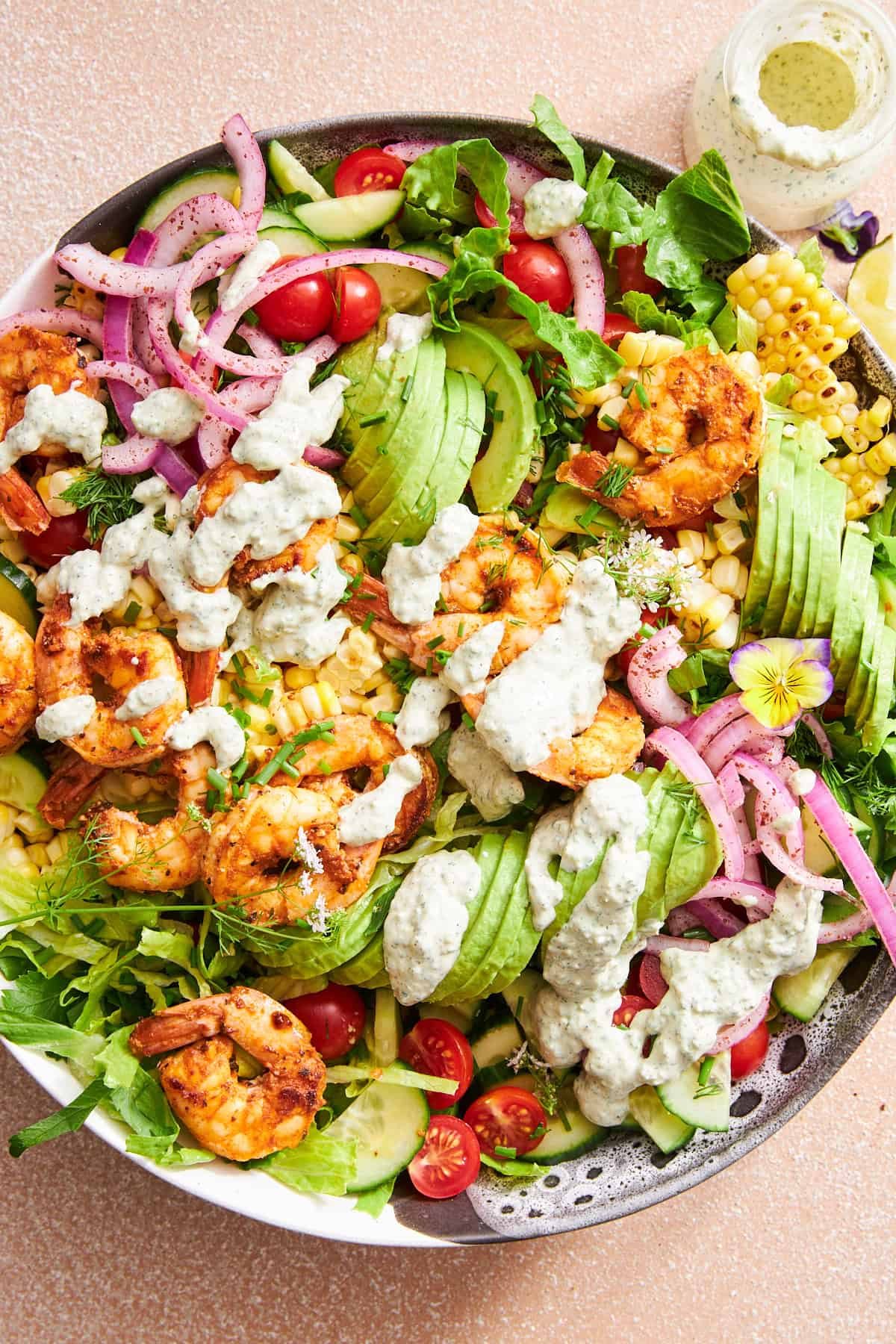 A bowl of shrimp avocado salad topped with creamy tahini dressing.