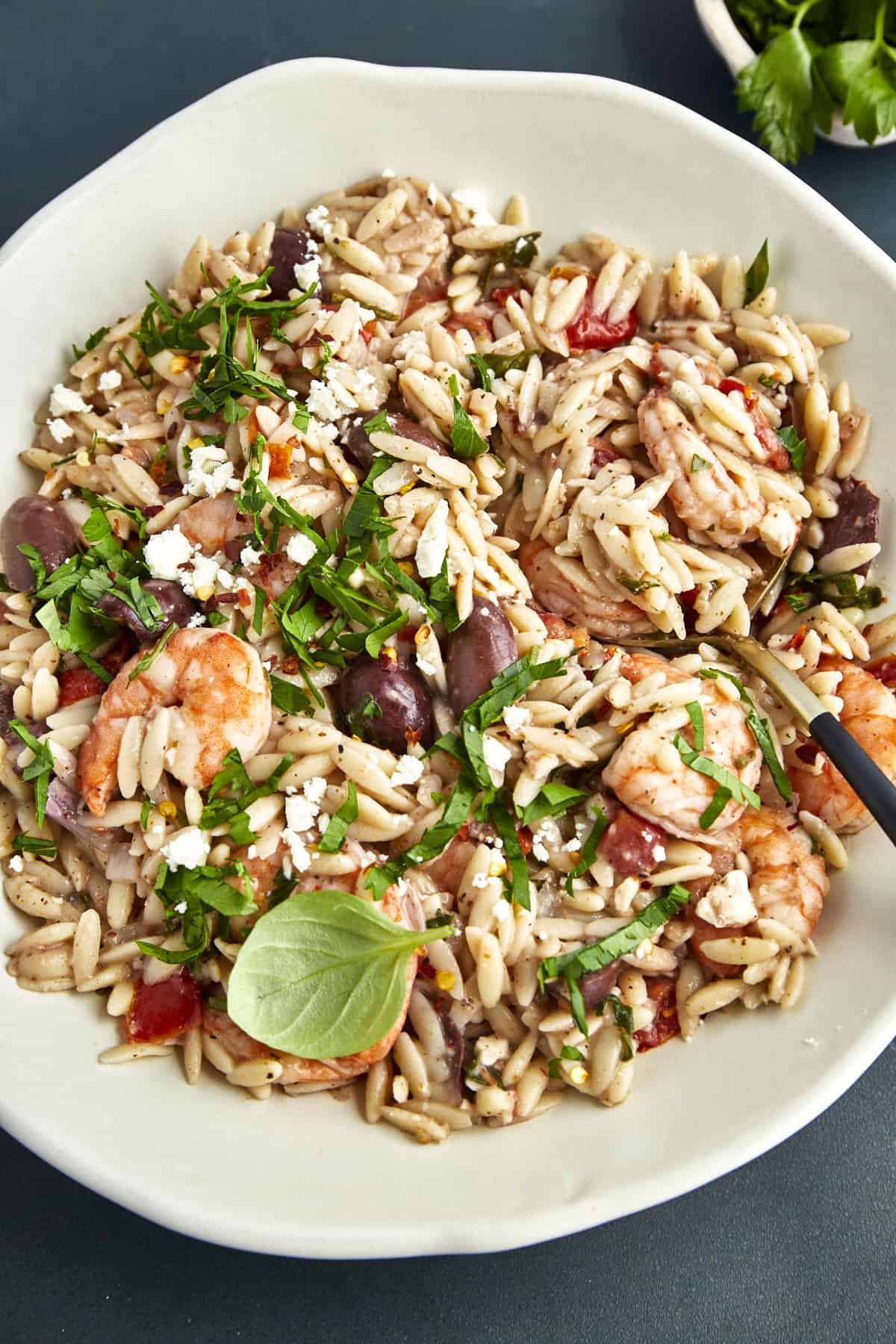 A bowl of shrimp and orzo with tomatoes, red onions, olives, fresh herbs, and feta.