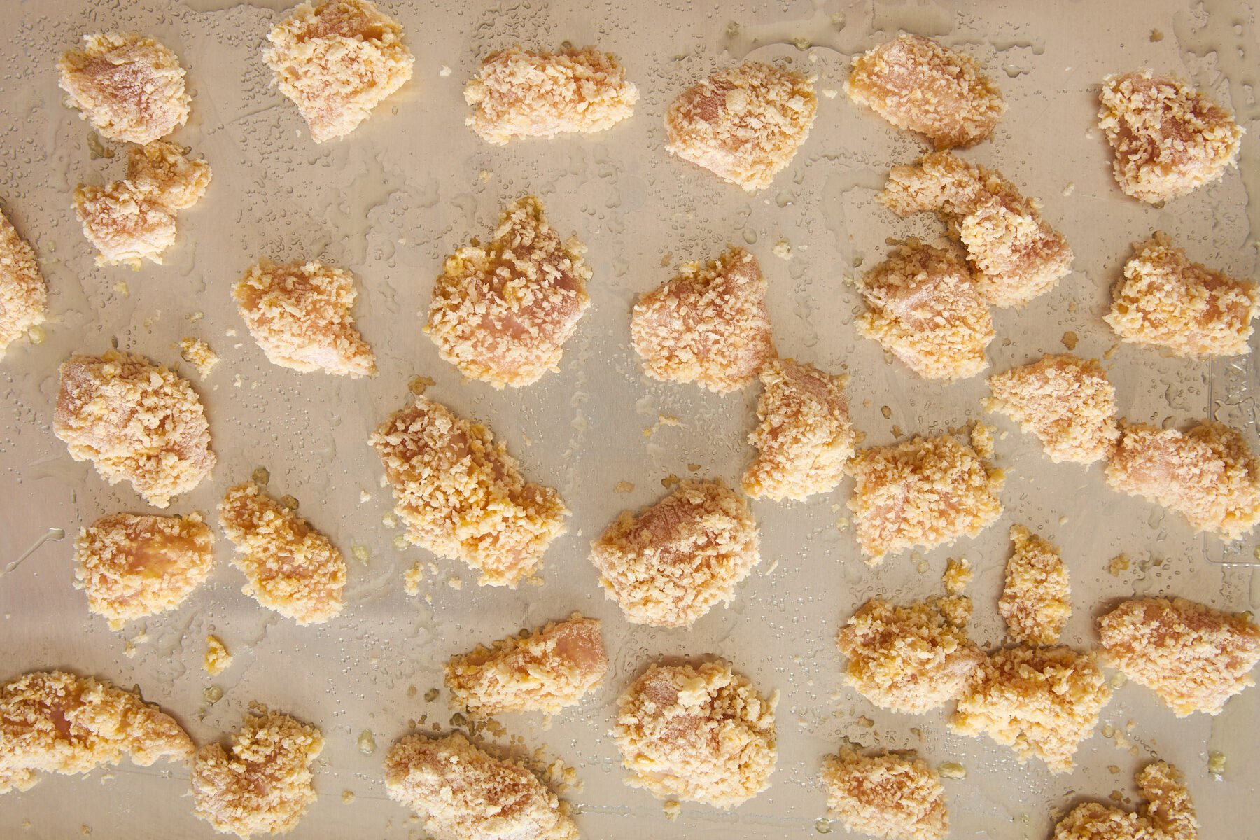 Raw breaded chicken pieces on a baking sheet.