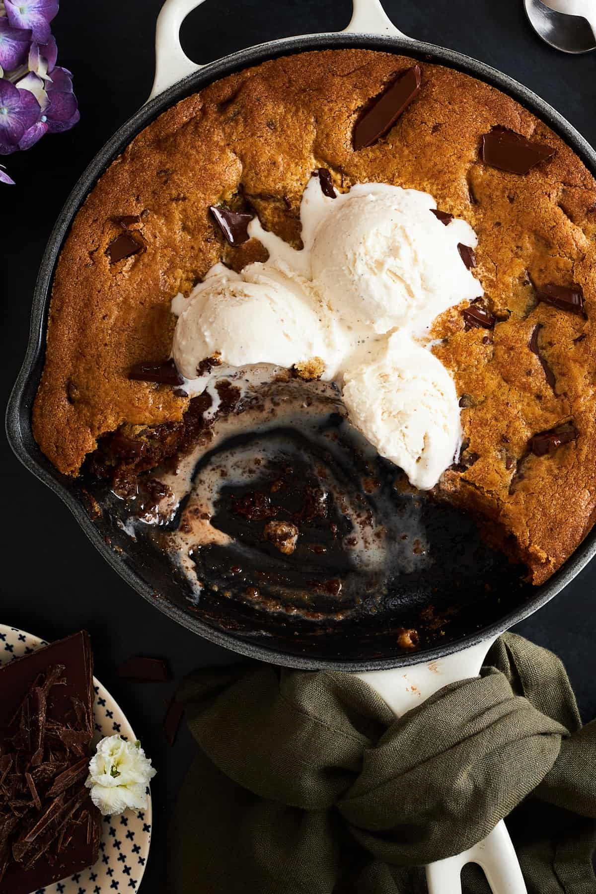 A chocolate chip skillet cookie topped with vanilla ice cream with bites missing.
